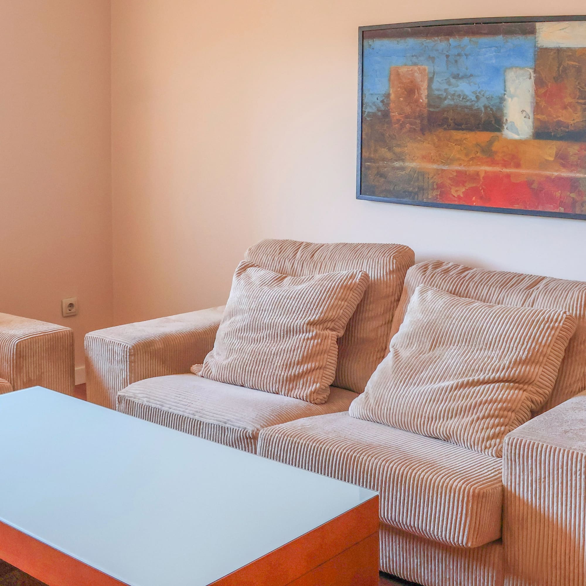 Modern living room with beige corduroy sofas, glass coffee table, and abstract art.
