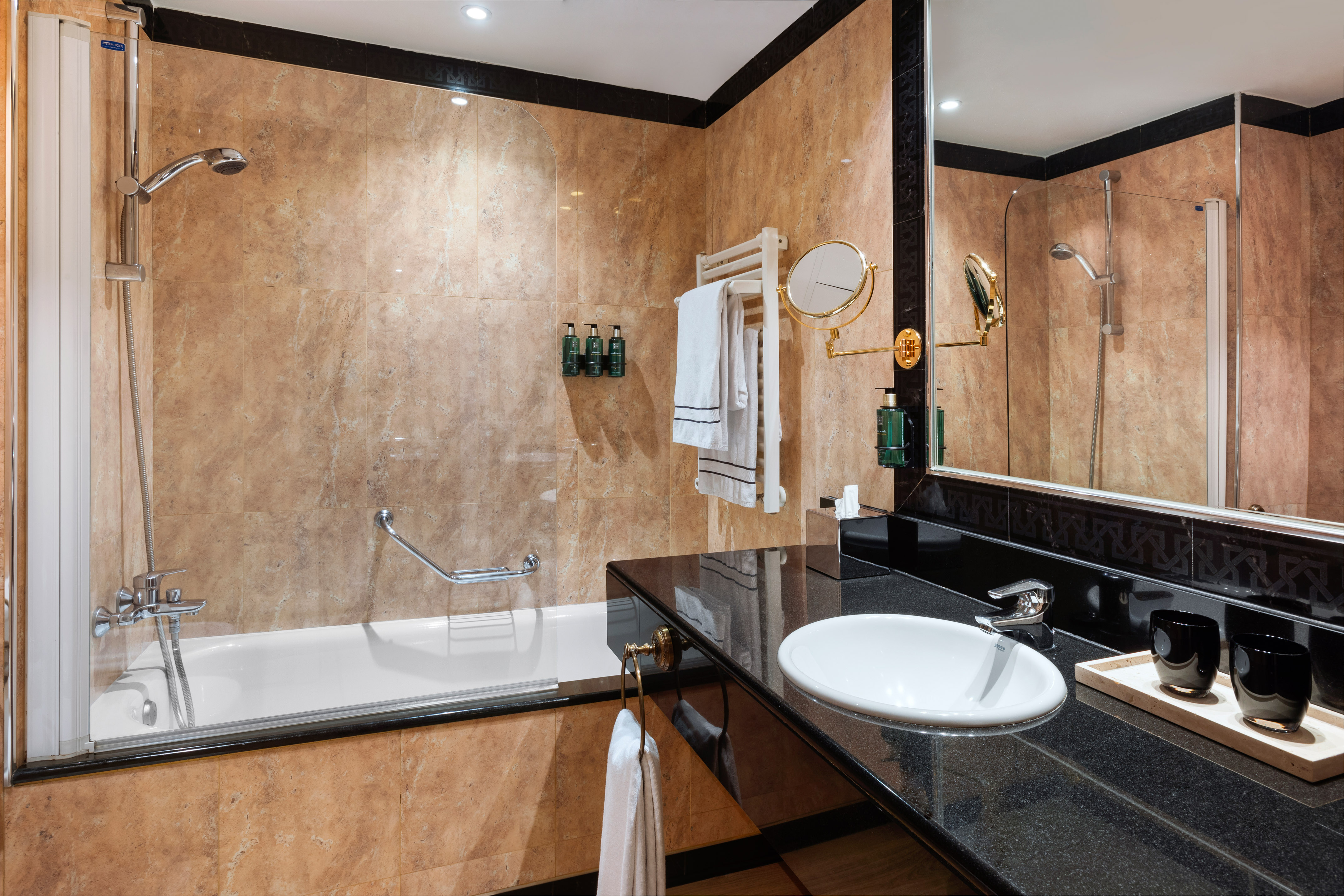 Modern hotel bathroom with black granite vanity, white sink, bathtub, and marble walls.