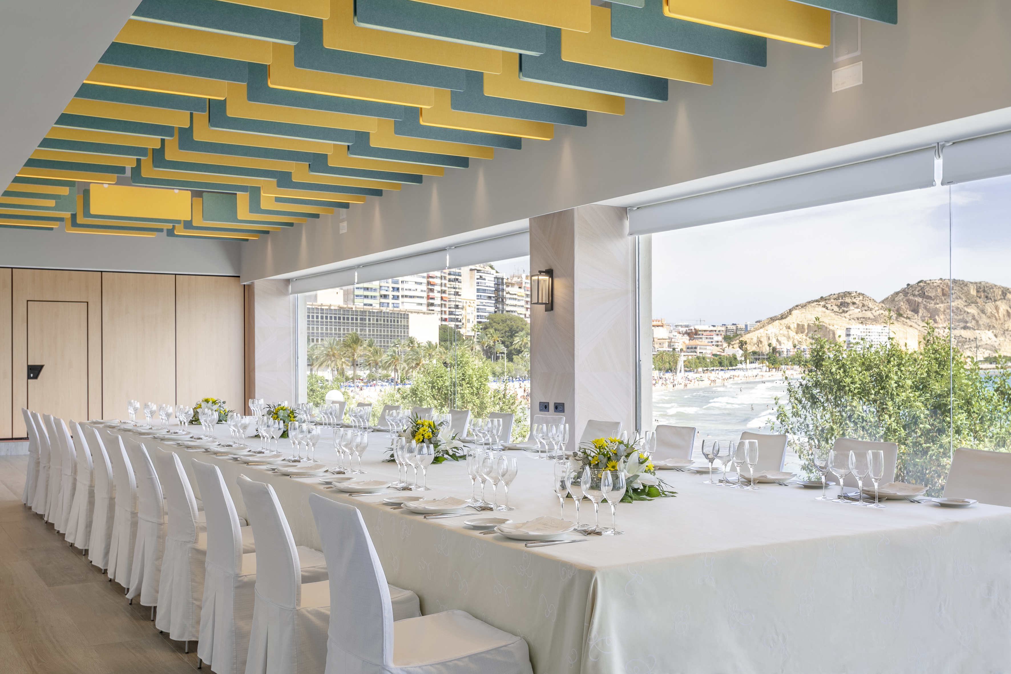 Modern event space with long dining table, white chairs, and panoramic sea view.