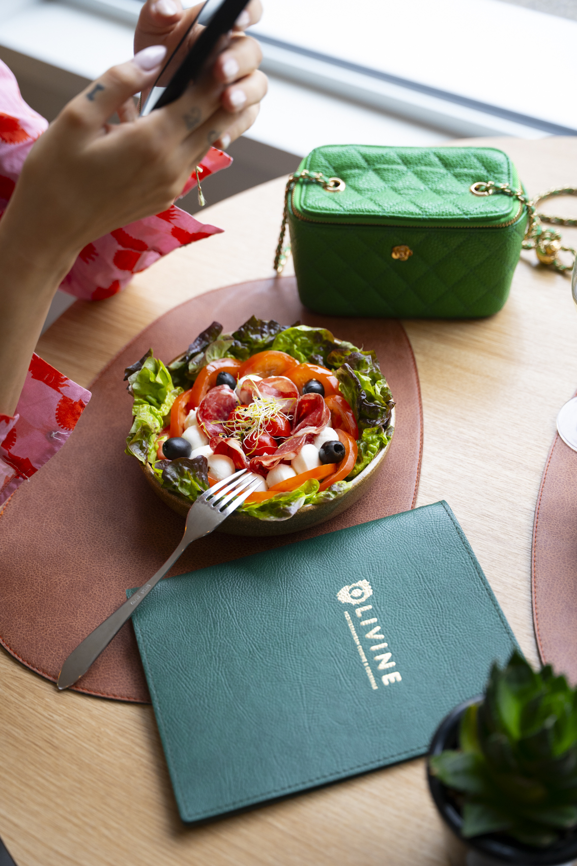 Fresh caprese salad with salami, Olivine menu, and green quilted handbag on a table.