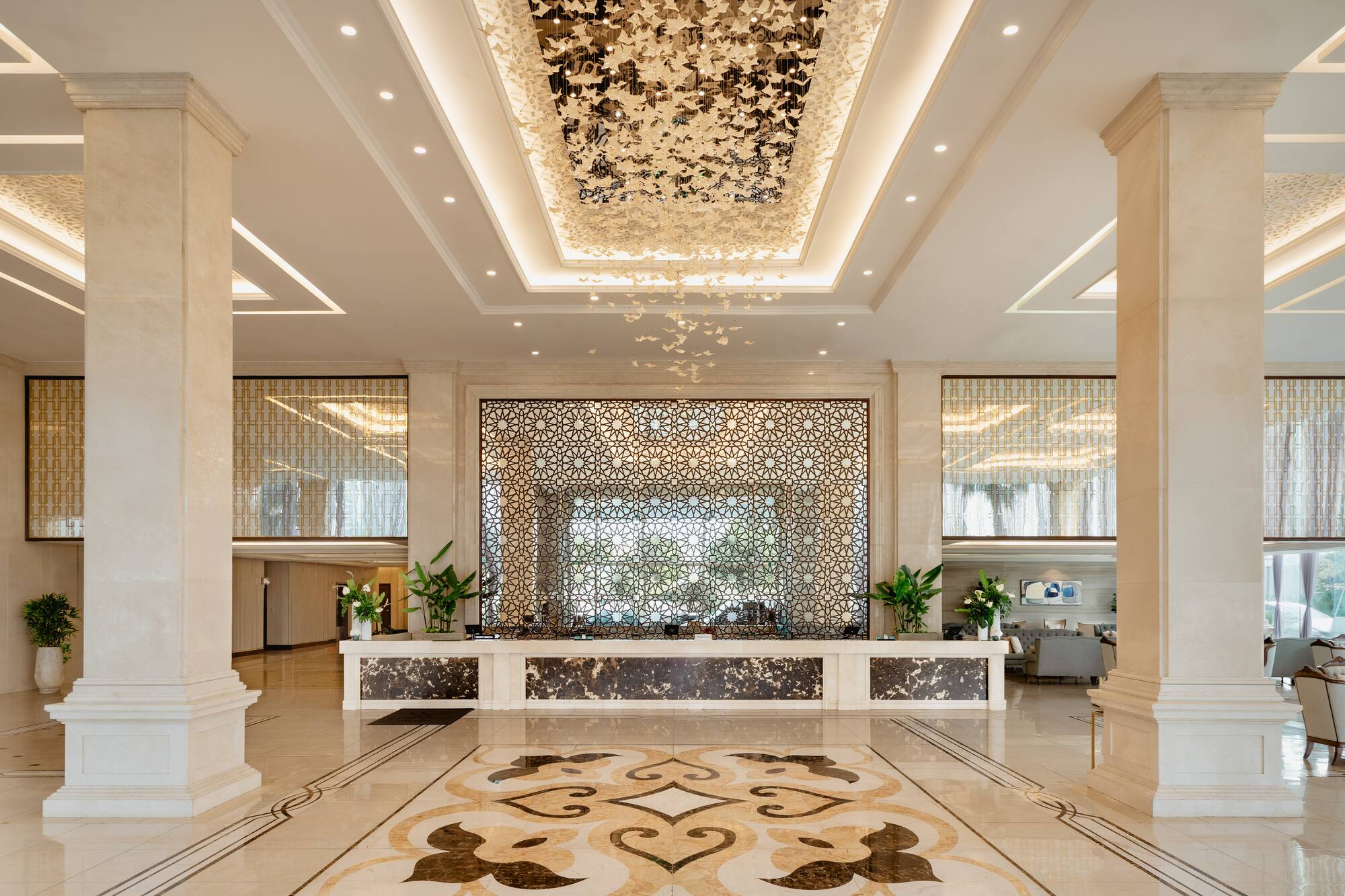 Hotel lobby with butterfly chandelier, marble, and geometric screen.
