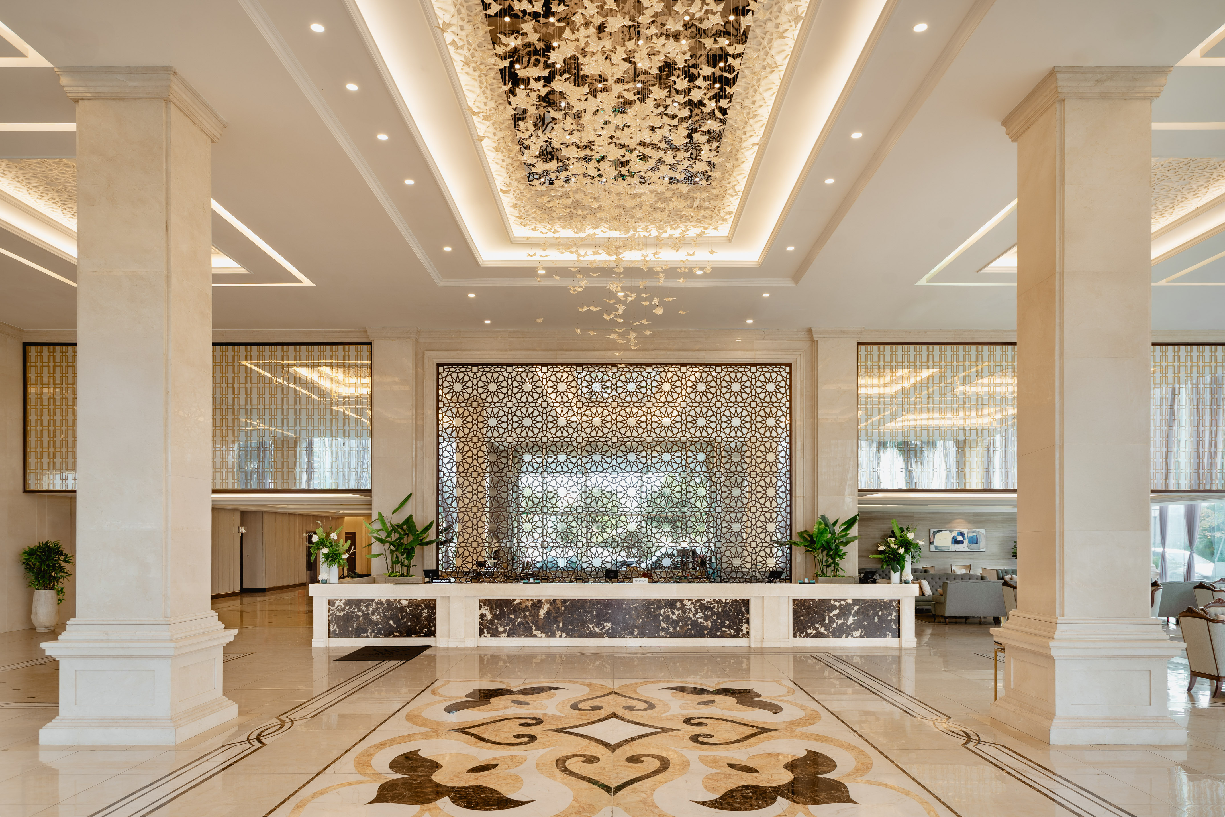 Hotel lobby with butterfly chandelier, marble, and geometric screen.