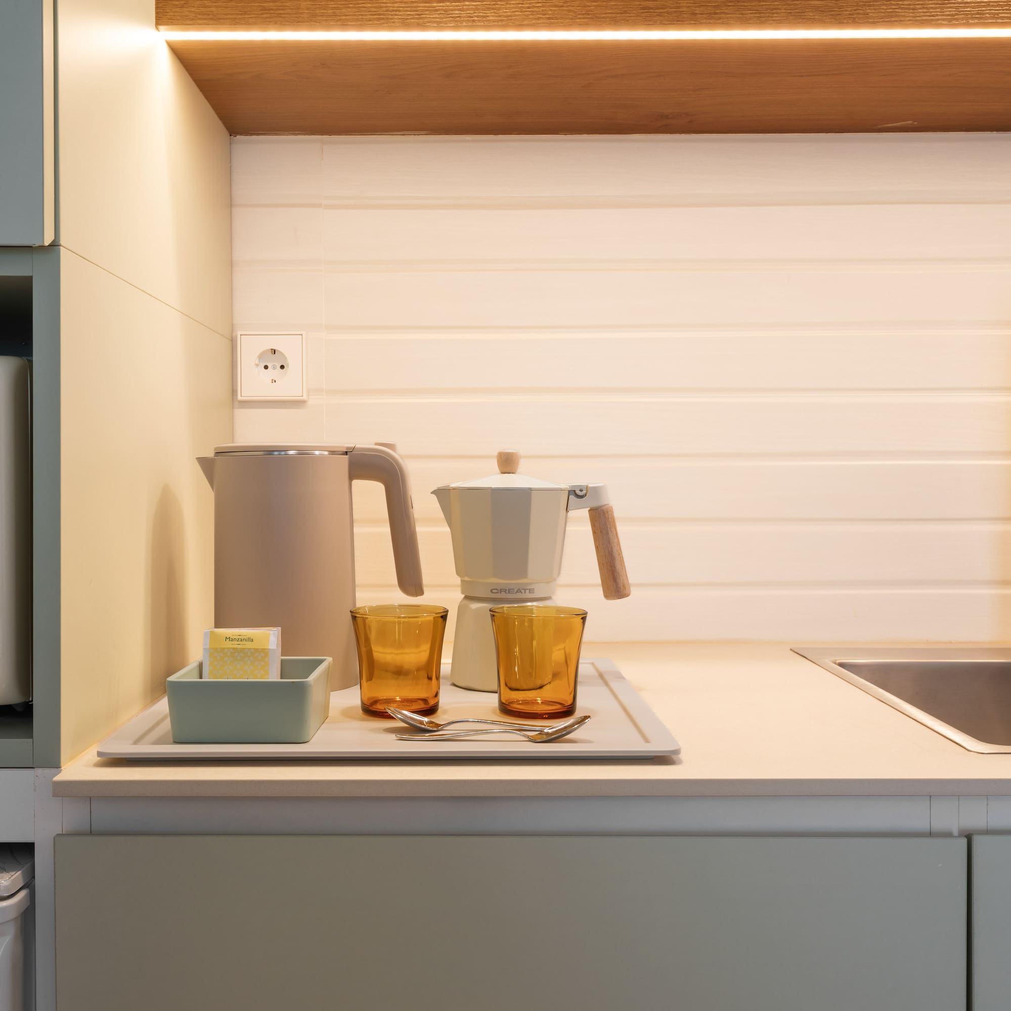 Modern compact kitchen with microwave, kettle, coffee maker, and sink.