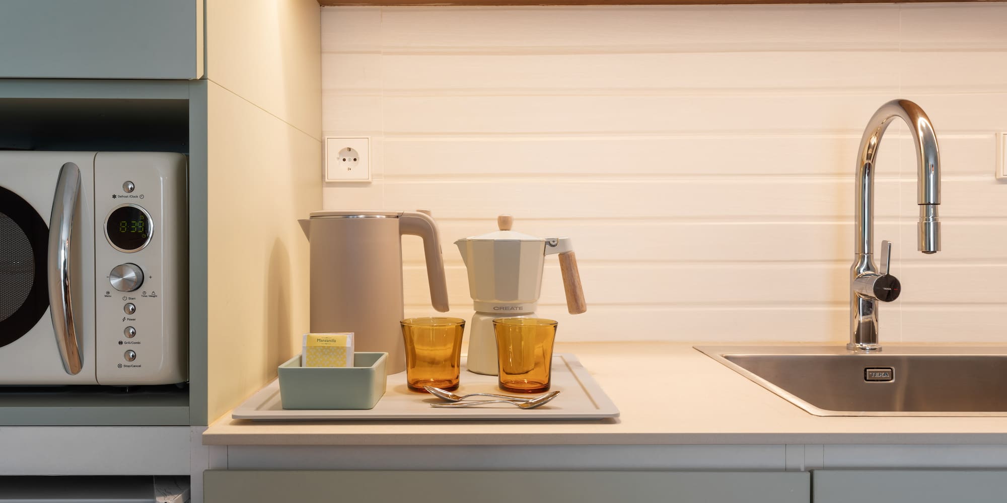 Modern compact kitchen with microwave, kettle, coffee maker, and sink.