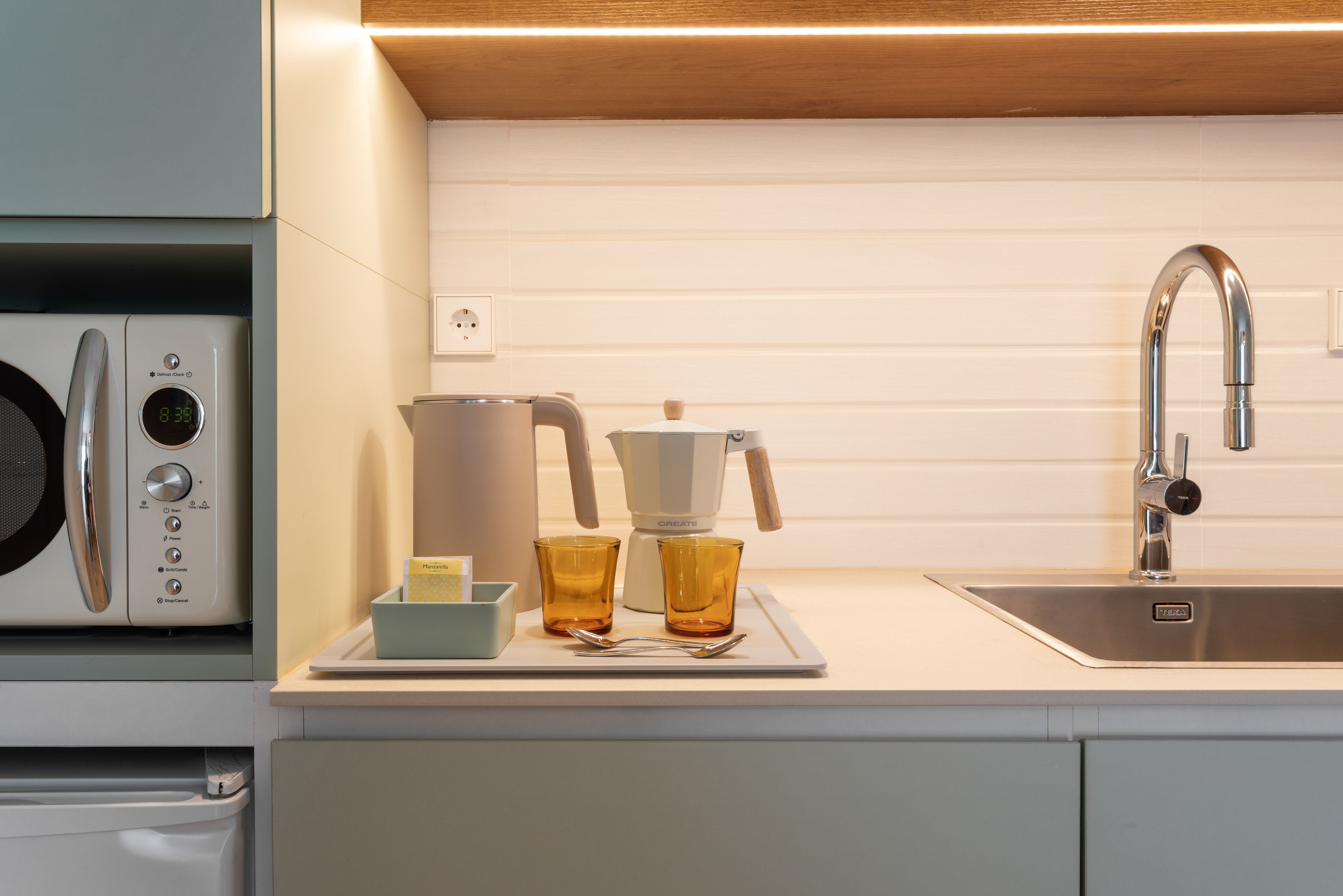 Modern kitchen counter with microwave, kettle, moka pot, sink, and tea setup.