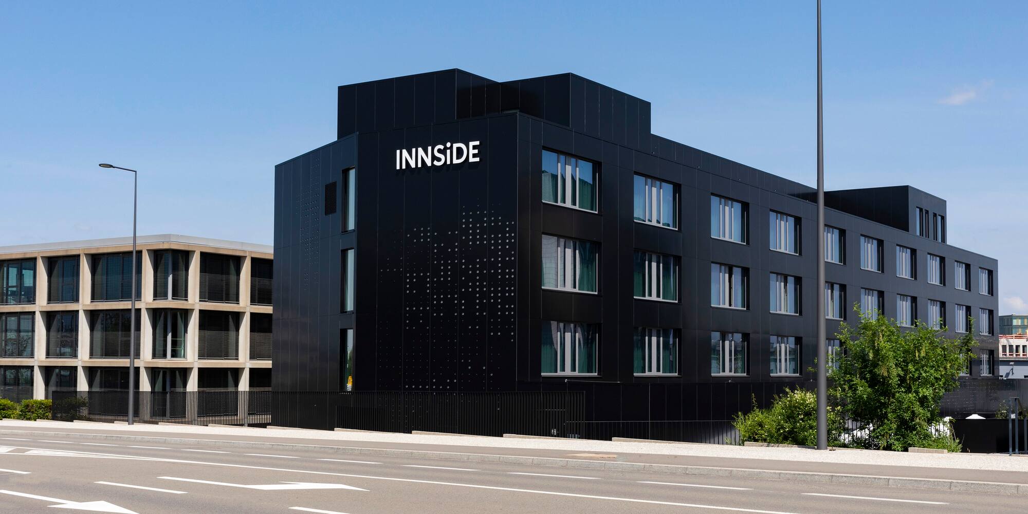 INNSiDE hotel: modern black building on a city street under blue sky.