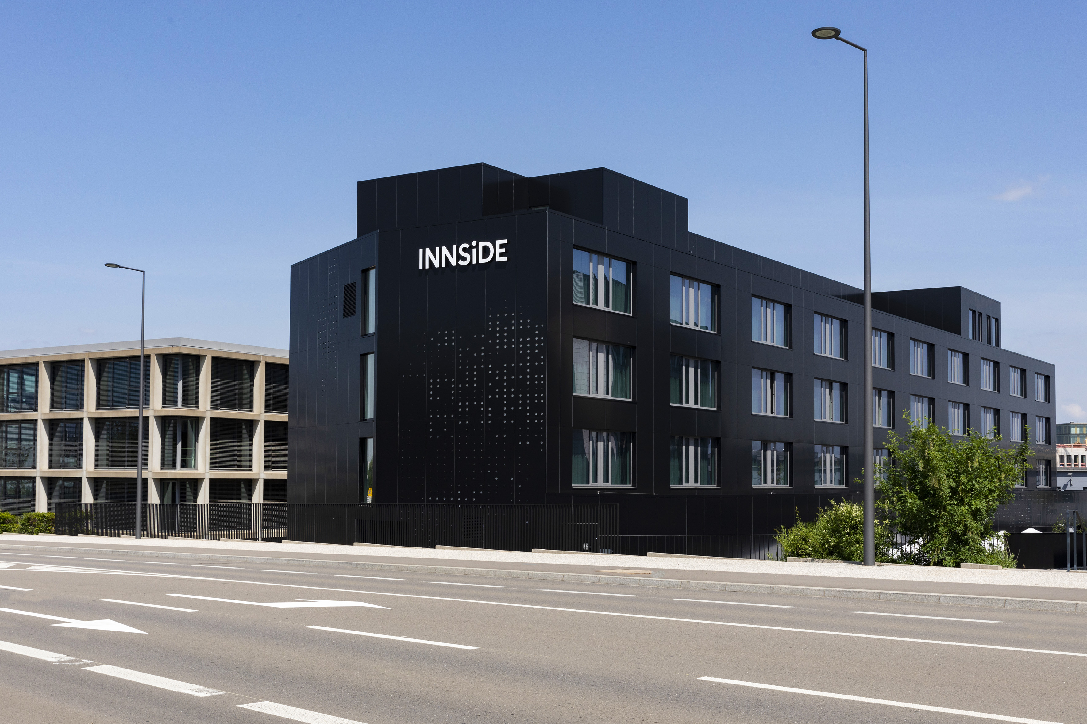 INNSiDE hotel: modern black building on a city street under blue sky.