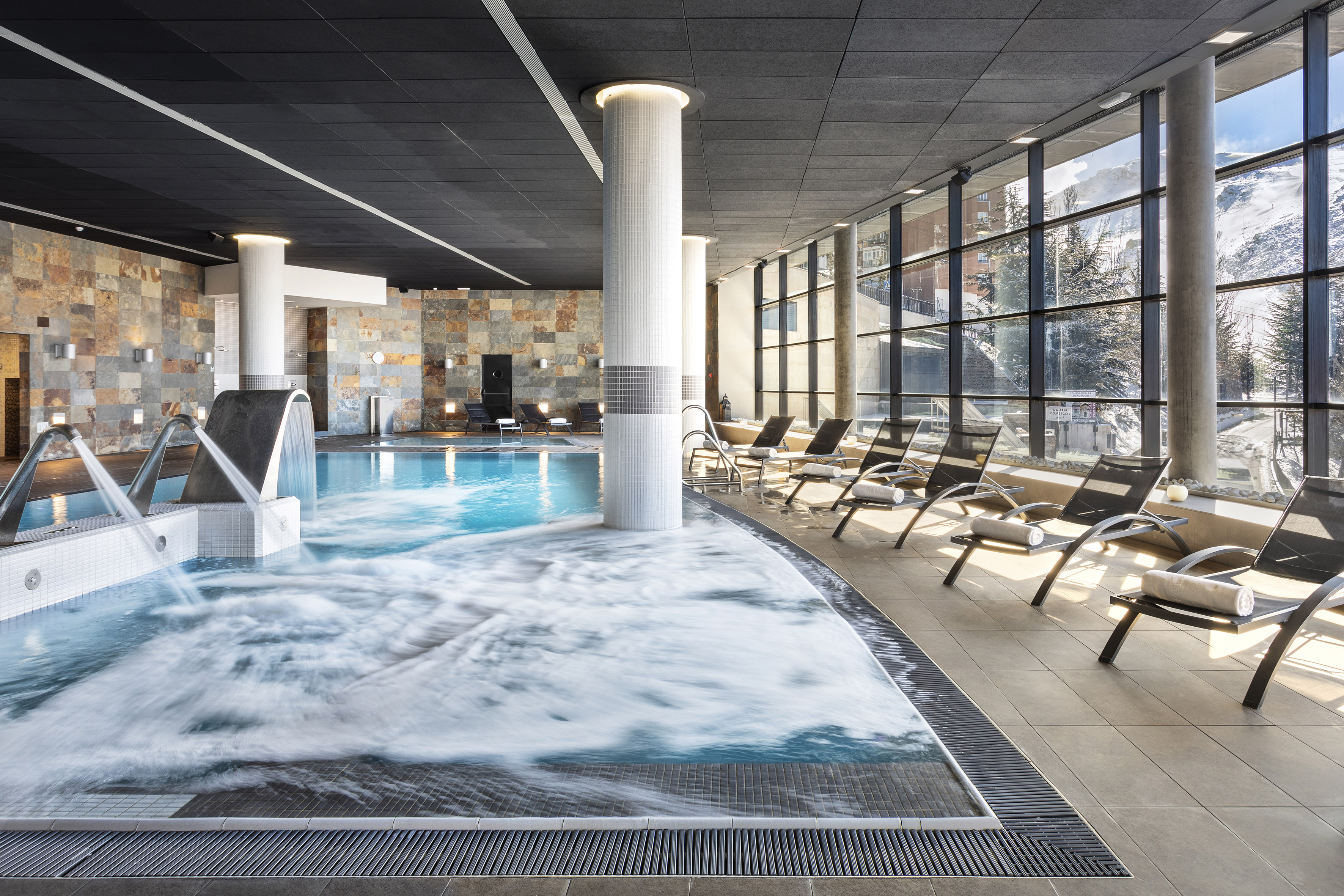 Mountain resort spa pool with bubbling jacuzzi and snowy window view.
