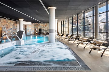 a pool with a waterfall and chairs in a room with windows