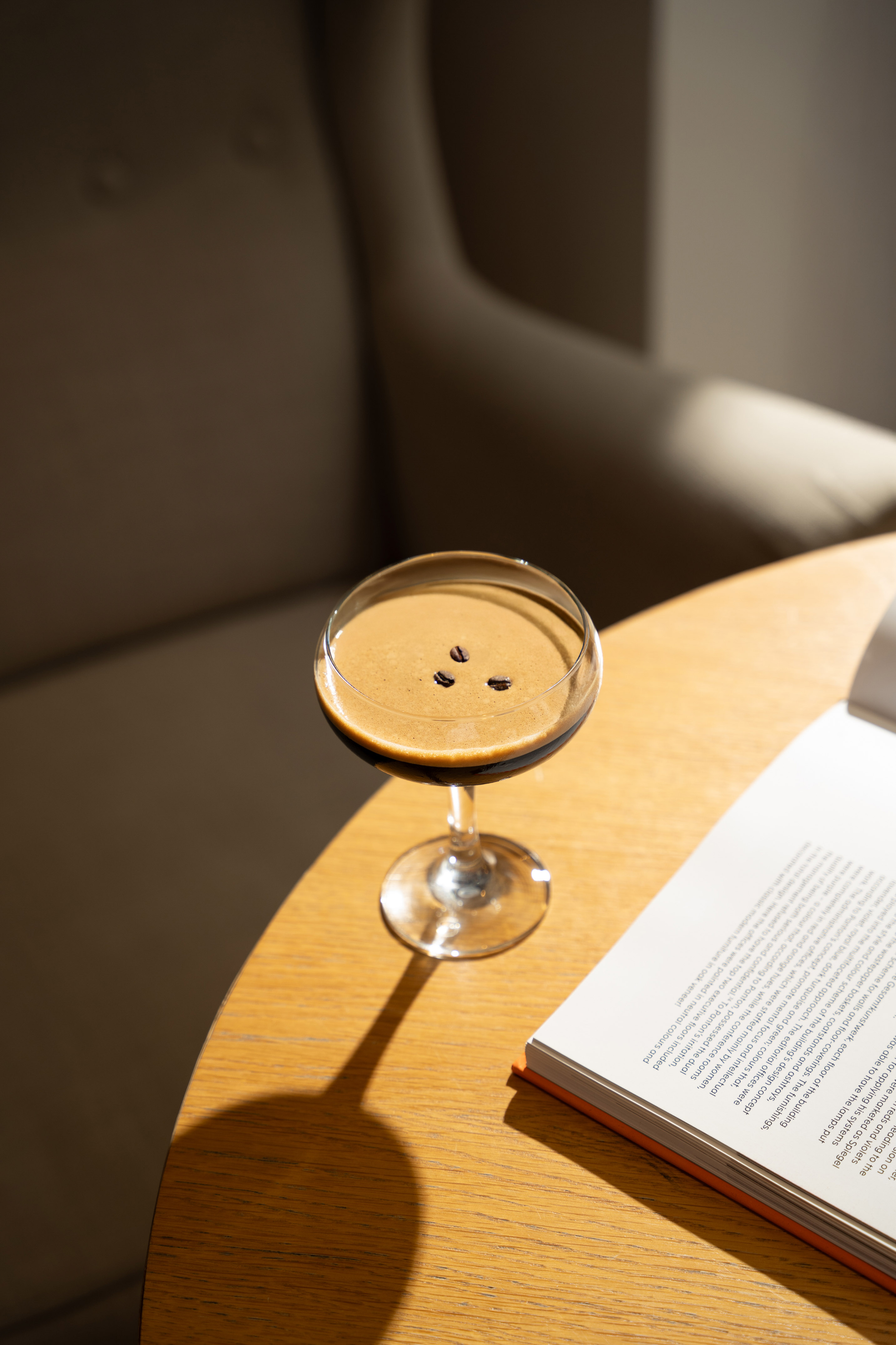 Espresso martini with coffee beans on a wooden table next to an open book.