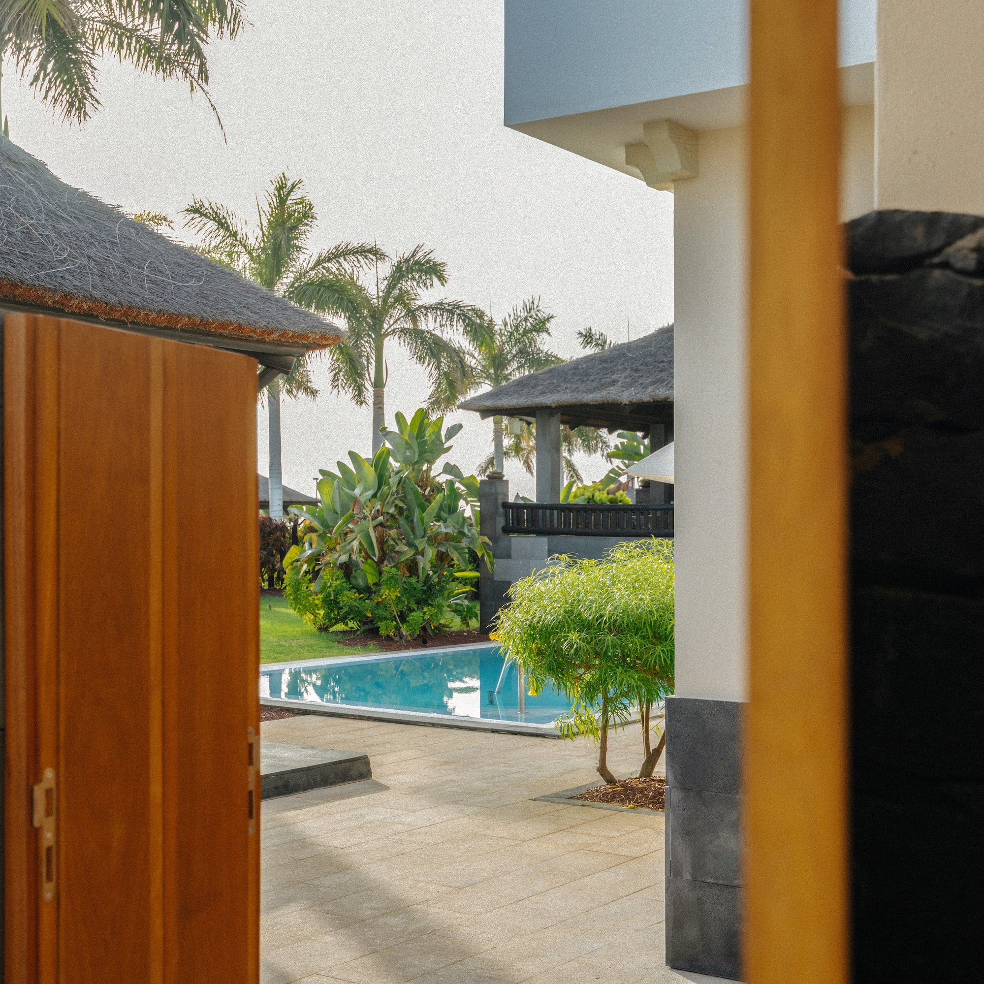 Tropical villa entrance with pool, garden, and palm trees.