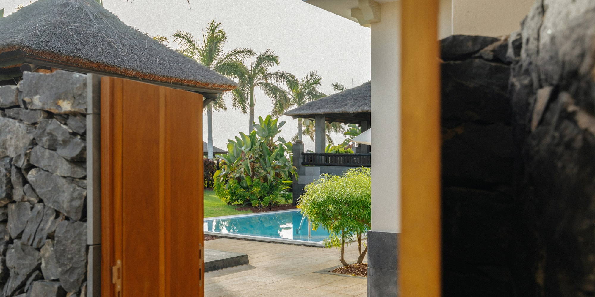 Tropical villa entrance with pool, garden, and palm trees.