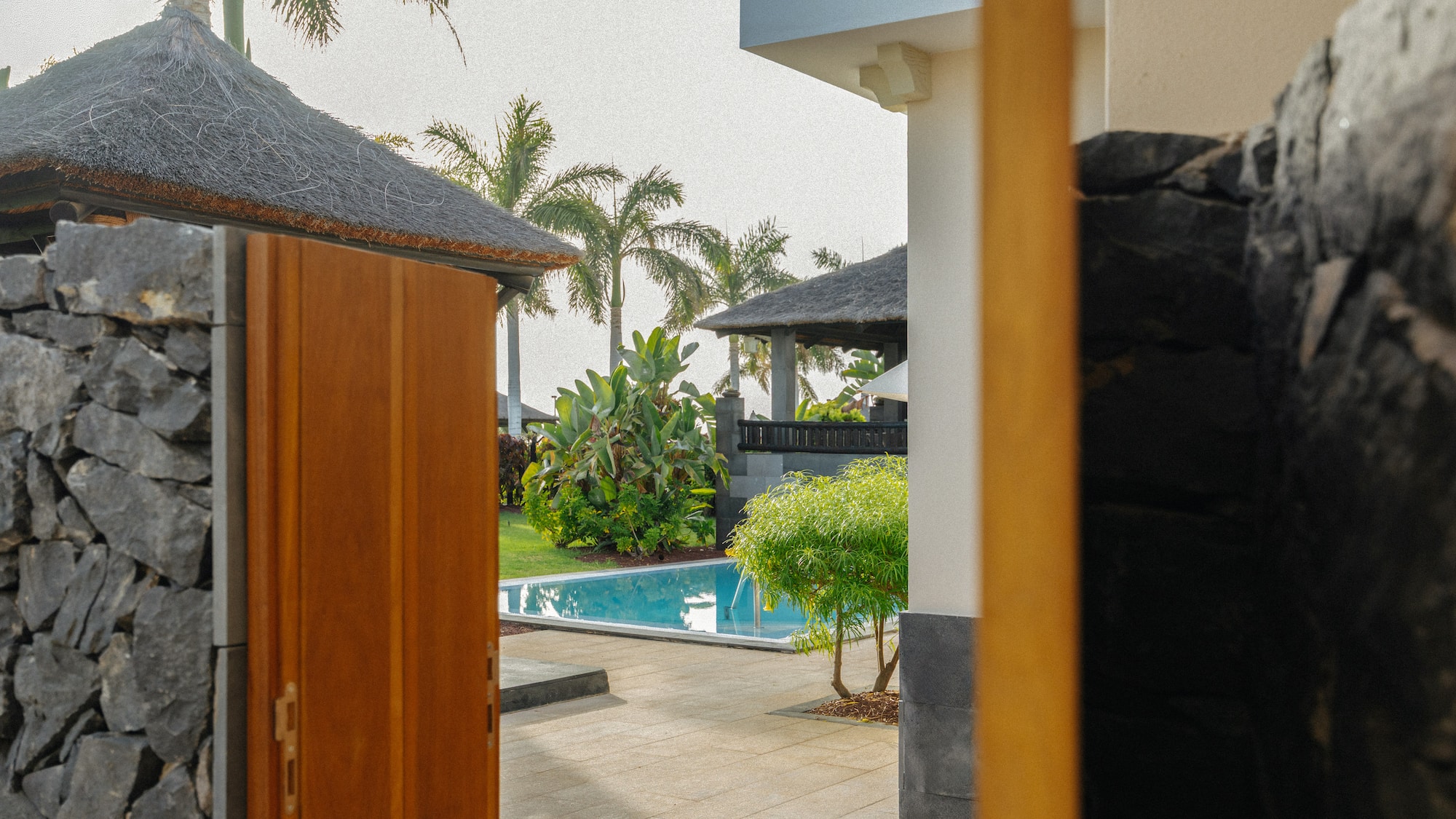 Tropical villa entrance with pool, garden, and palm trees.