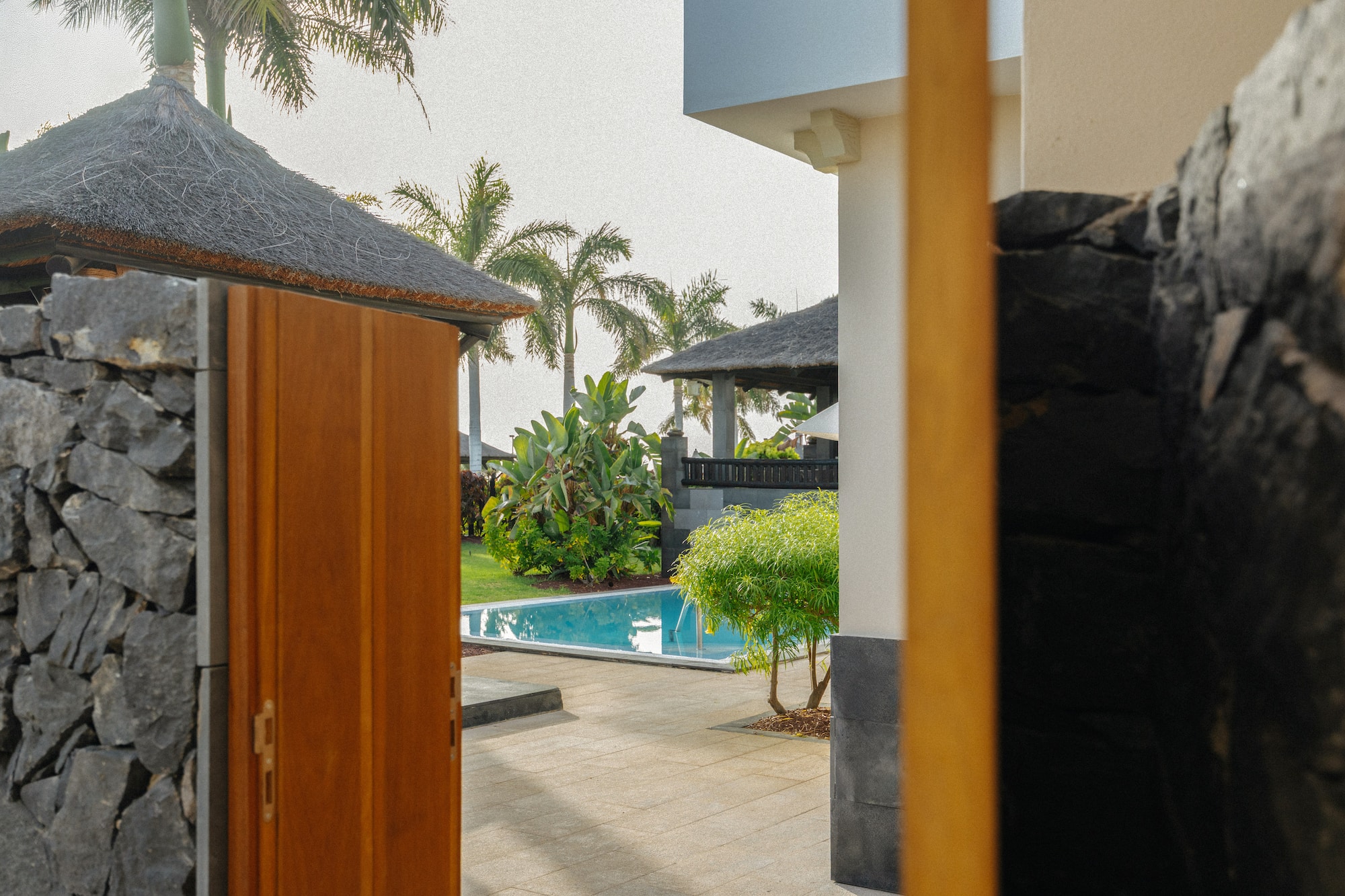 Tropical villa entrance with pool, garden, and palm trees.
