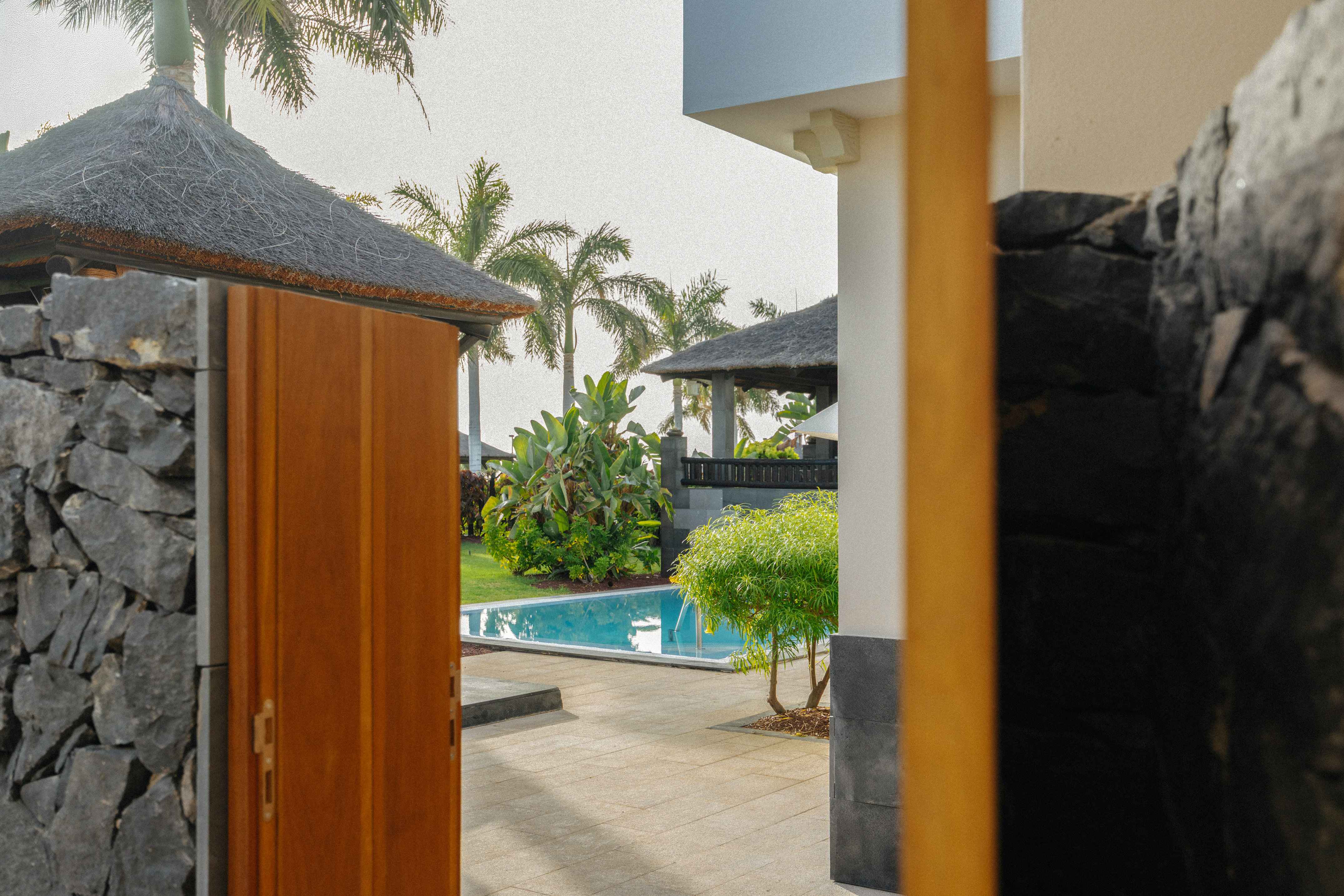 Tropical villa entrance with pool, garden, and palm trees.