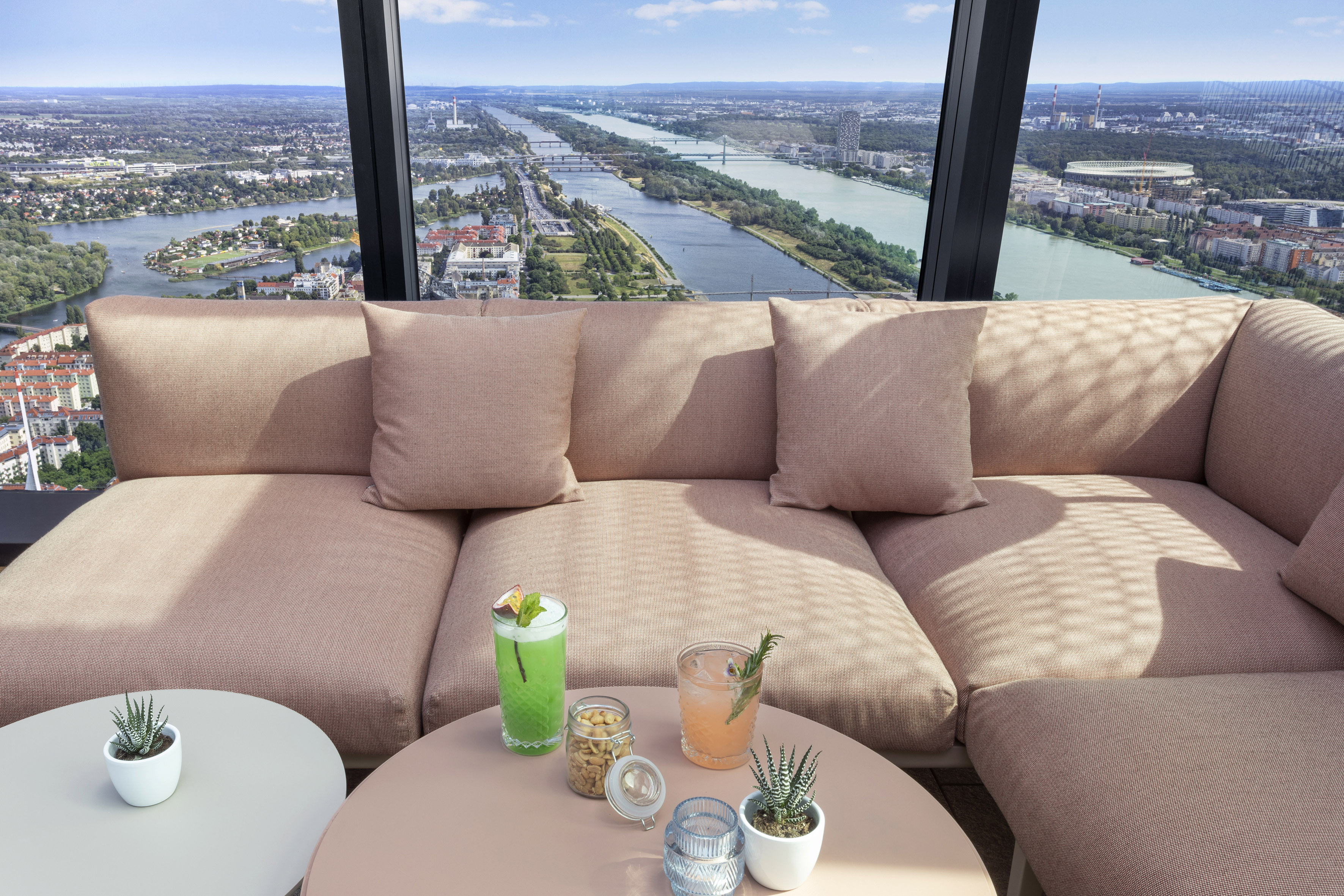 Rooftop lounge: pink sofa, cocktails, panoramic Vienna city and Danube river view.