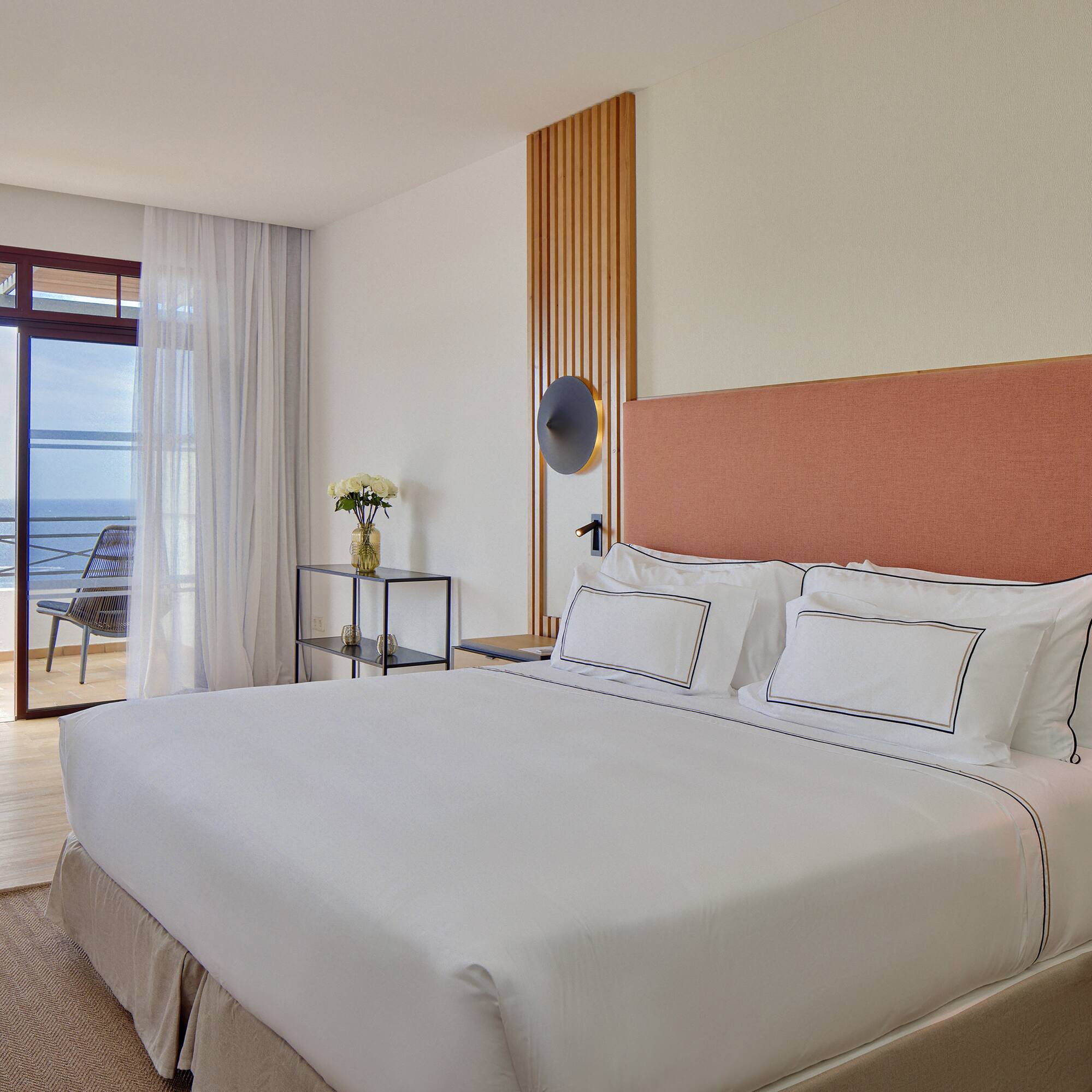a bed with white sheets and a glass table next to a window