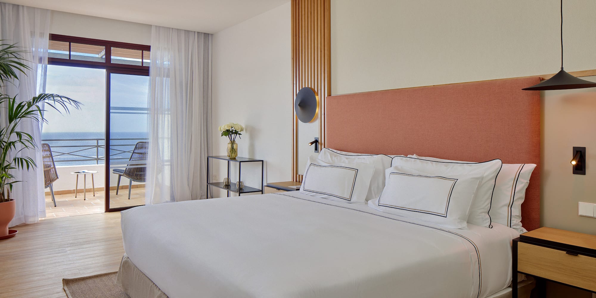 a bed with white sheets and a glass table next to a window