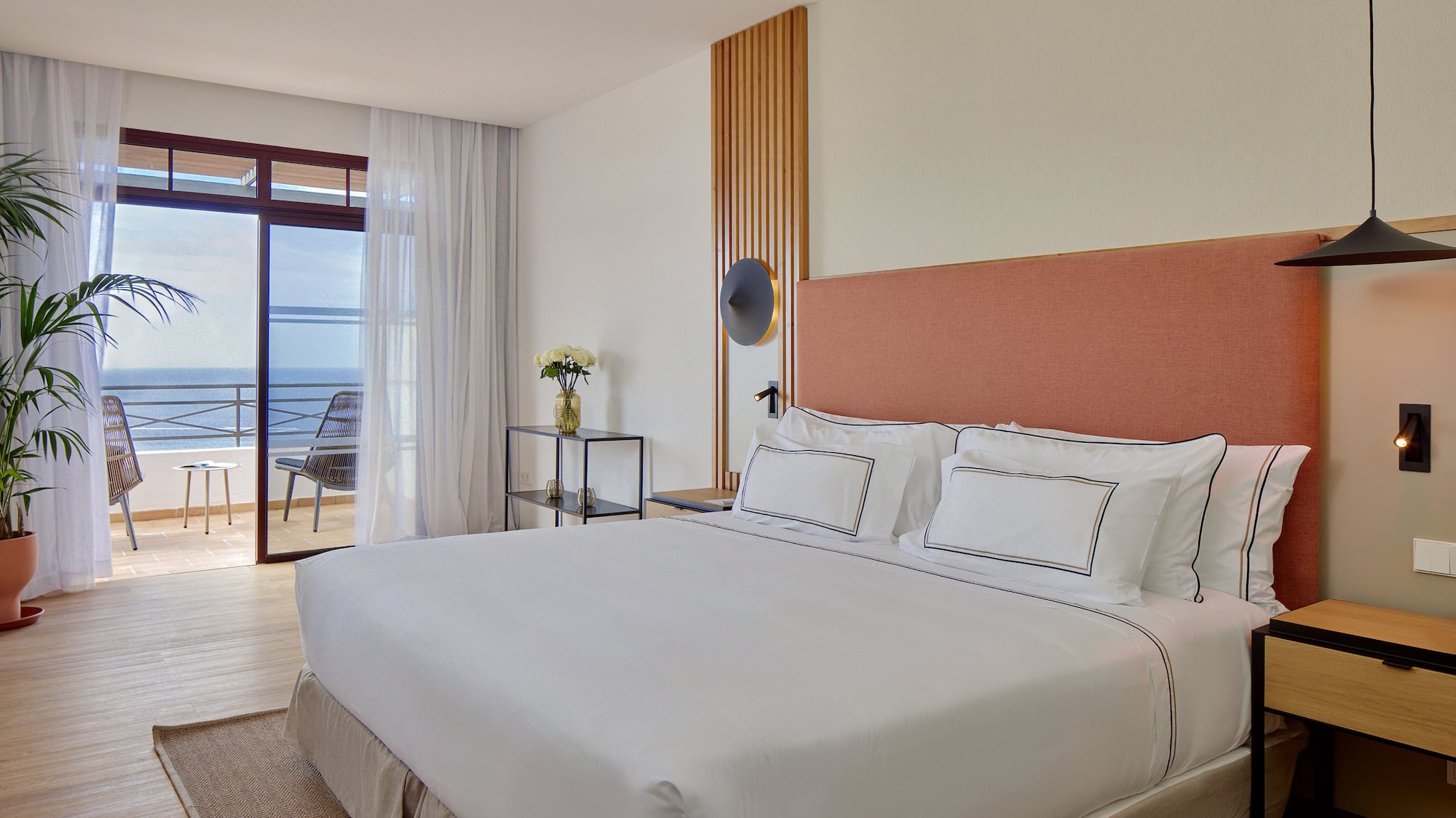 a bed with white sheets and a glass table next to a window