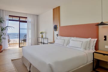 a bed with white sheets and a glass table next to a window