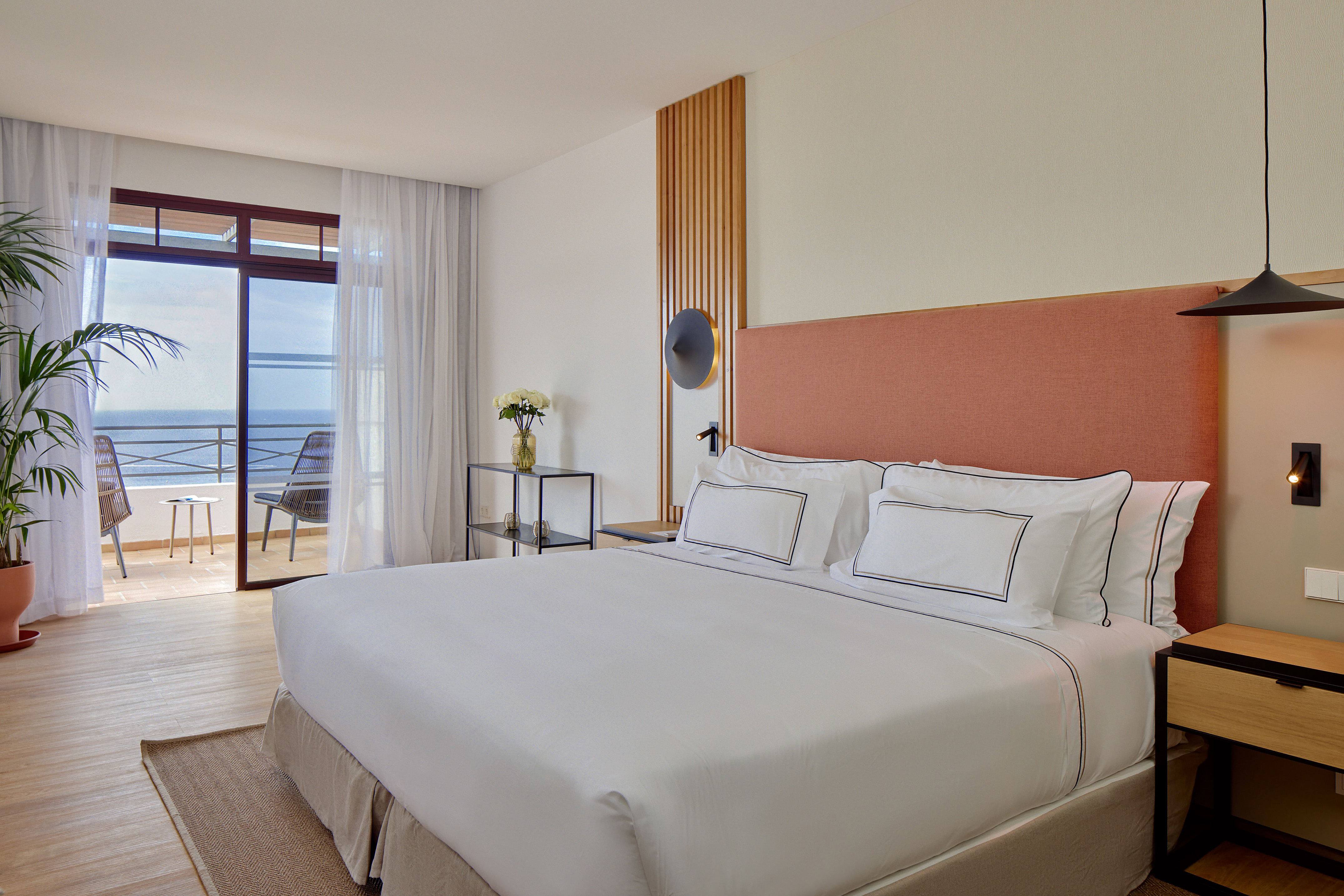 Coastal hotel bedroom with ocean view balcony, king bed, modern decor.