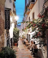 people sitting at tables in a narrow alley between buildings