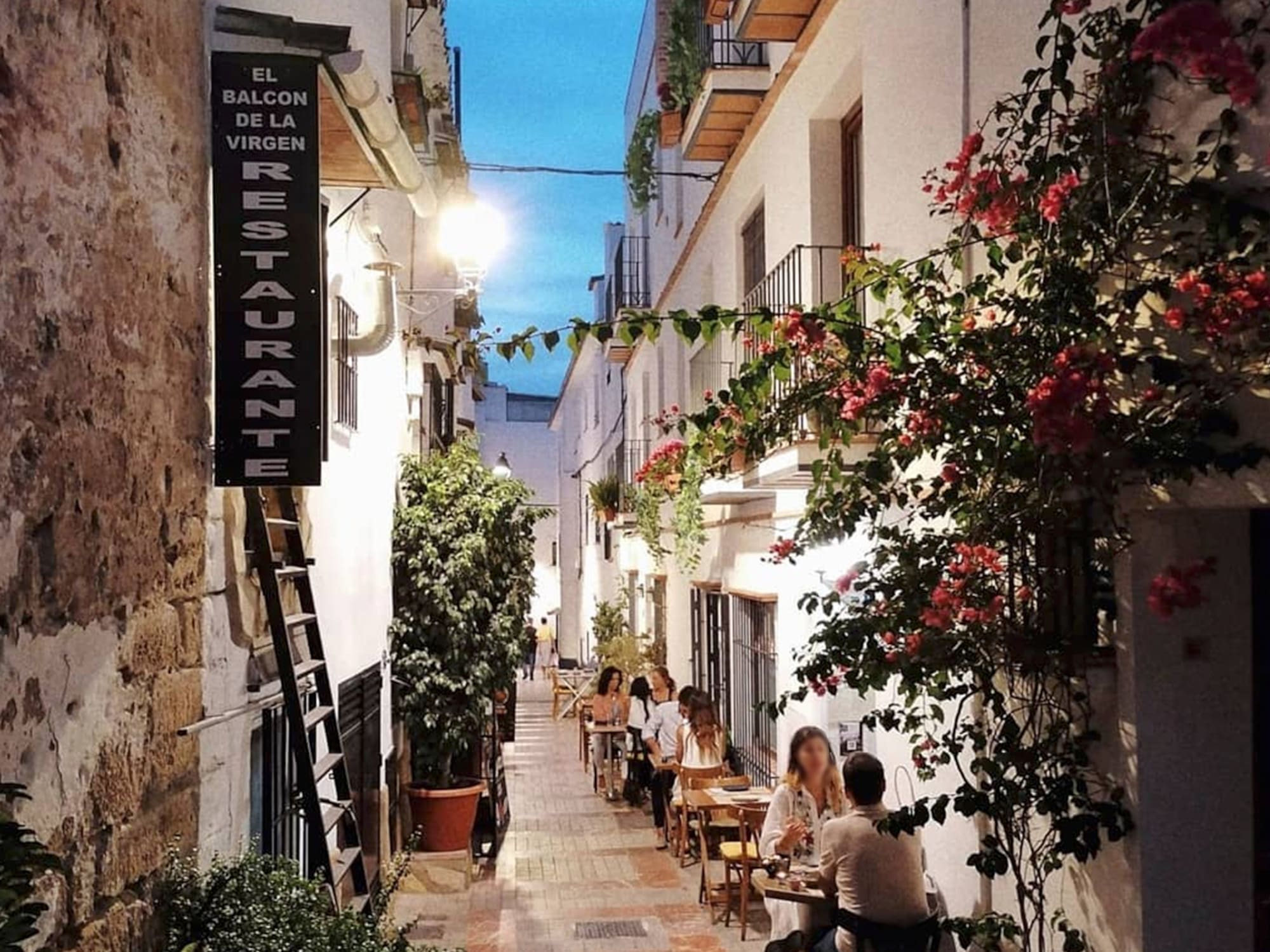 people sitting at tables in a narrow alley between buildings