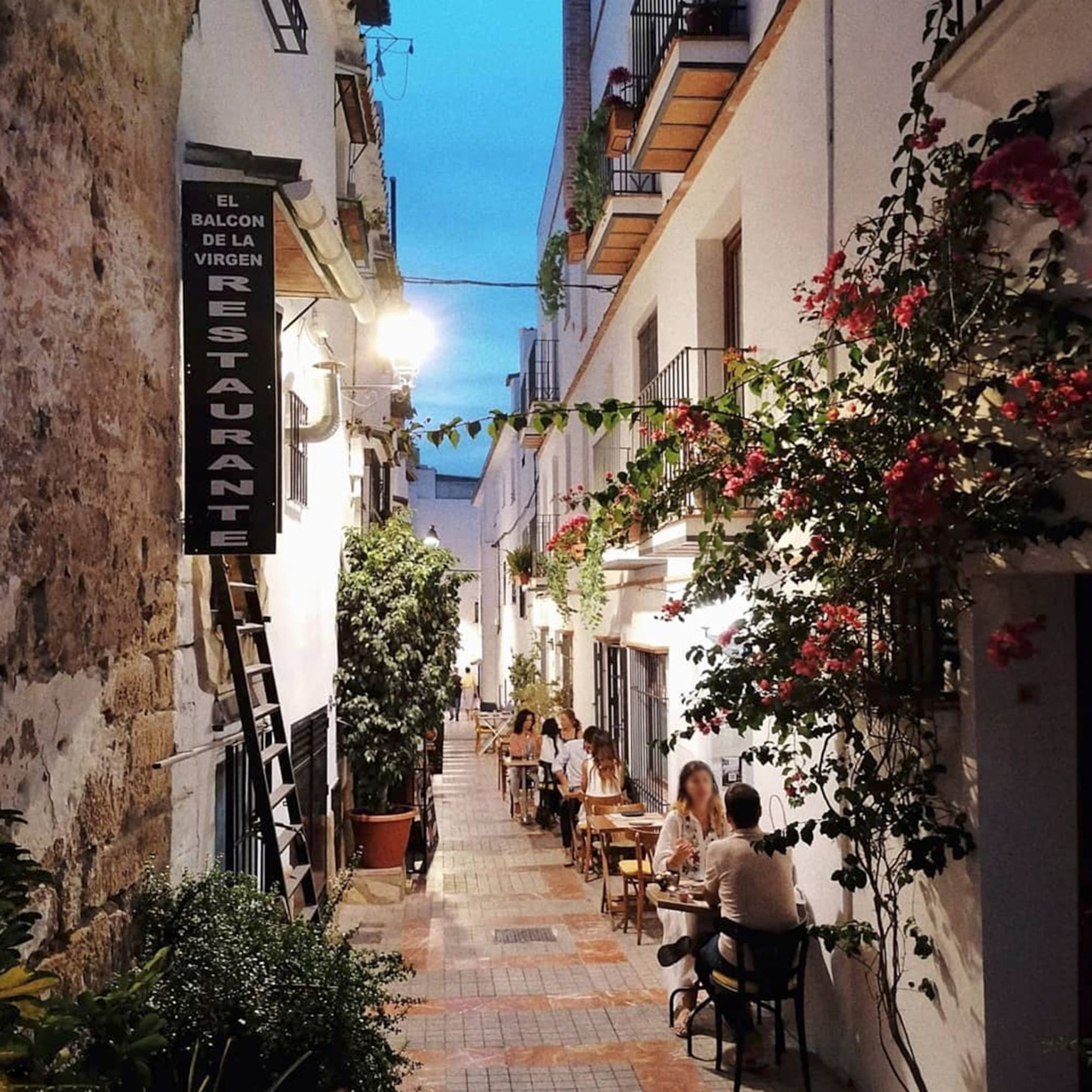 people sitting at tables in a narrow alley between buildings