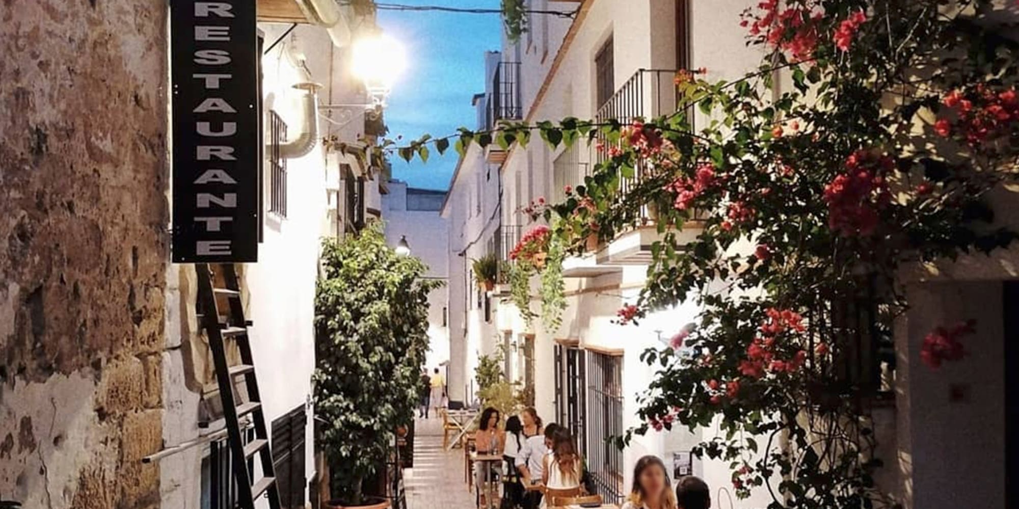 people sitting at tables in a narrow alley between buildings