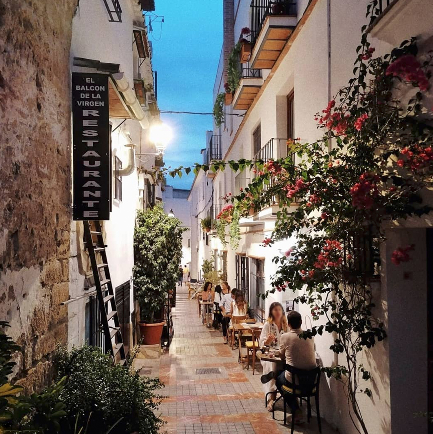 people sitting at tables in a narrow alley between buildings