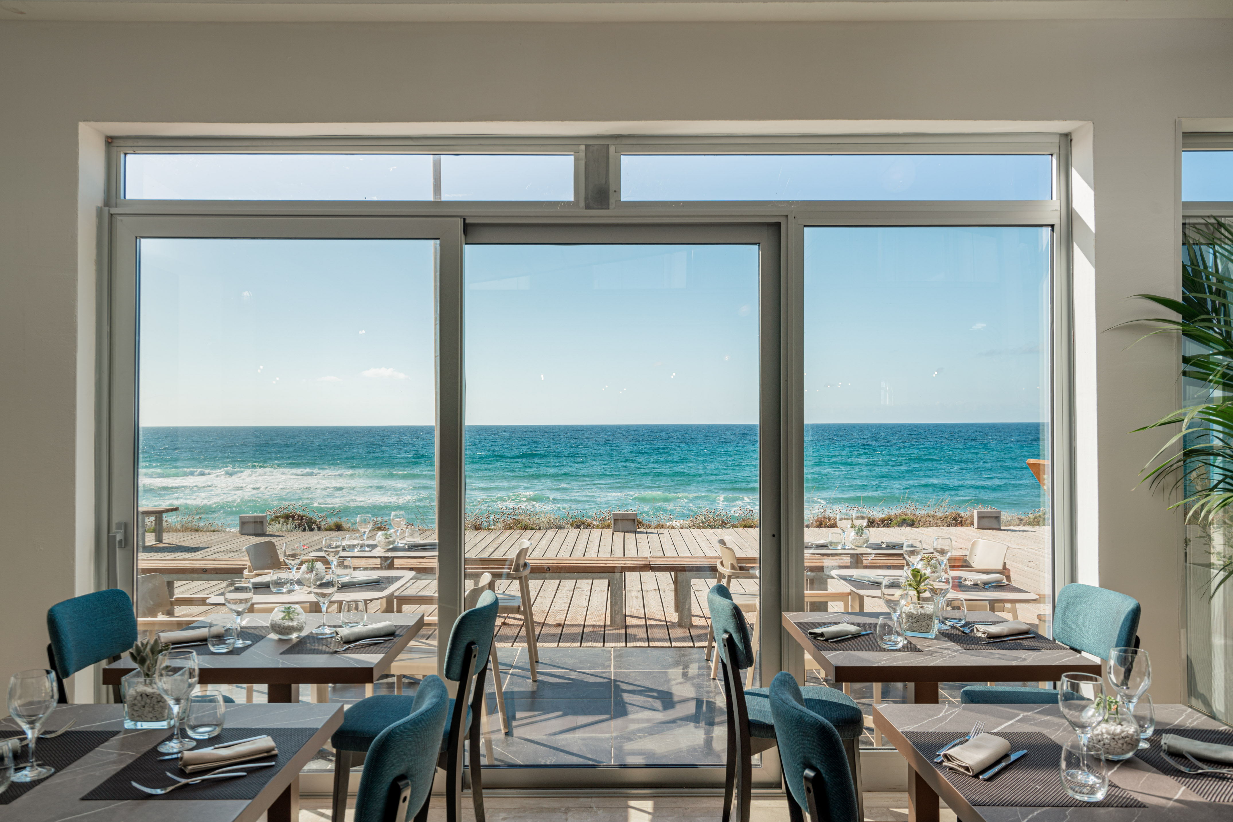 Coastal restaurant dining room with panoramic sea view and set tables.