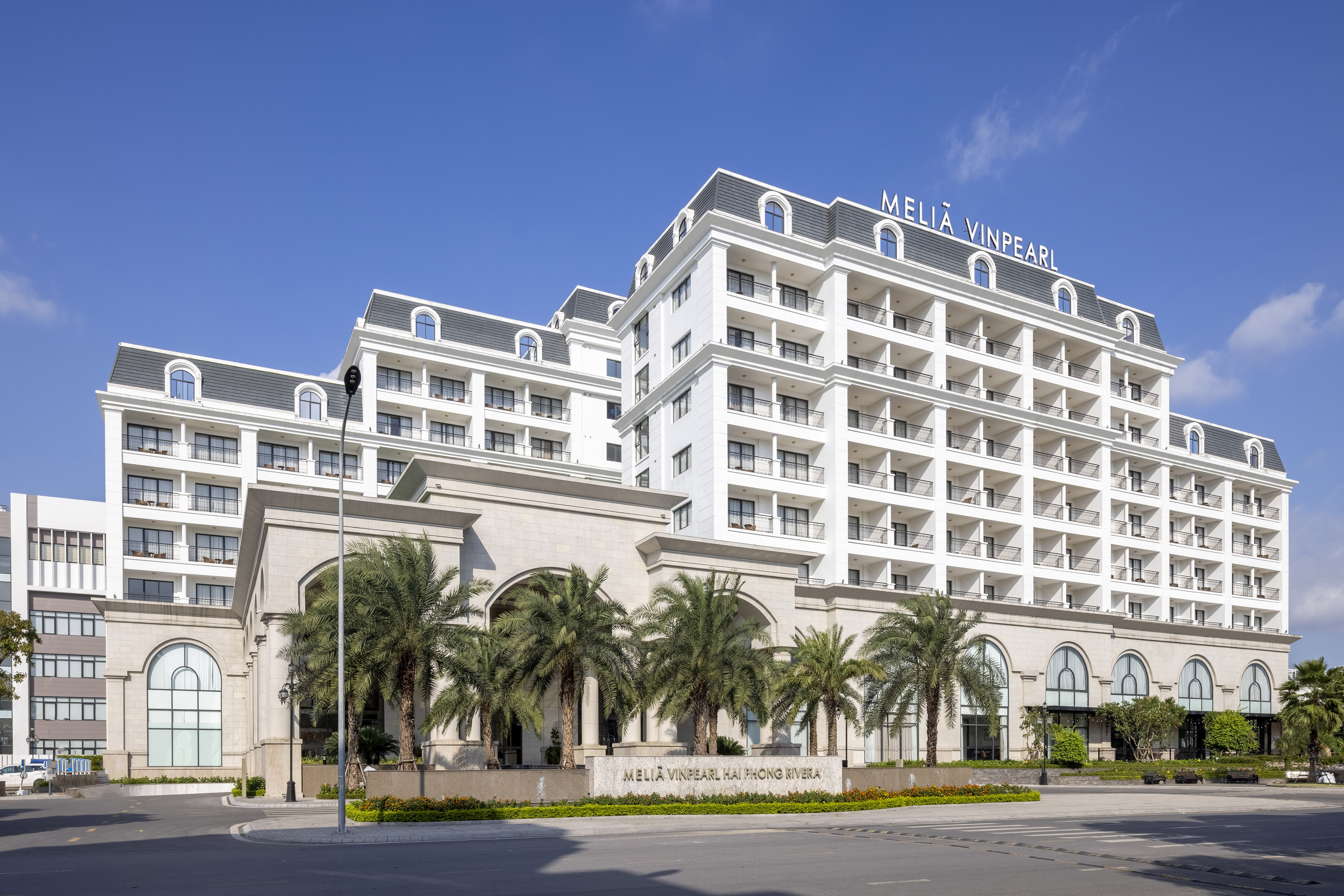 Melia Vinpearl Hai Phong Rivera hotel facade with palm trees and blue sky.
