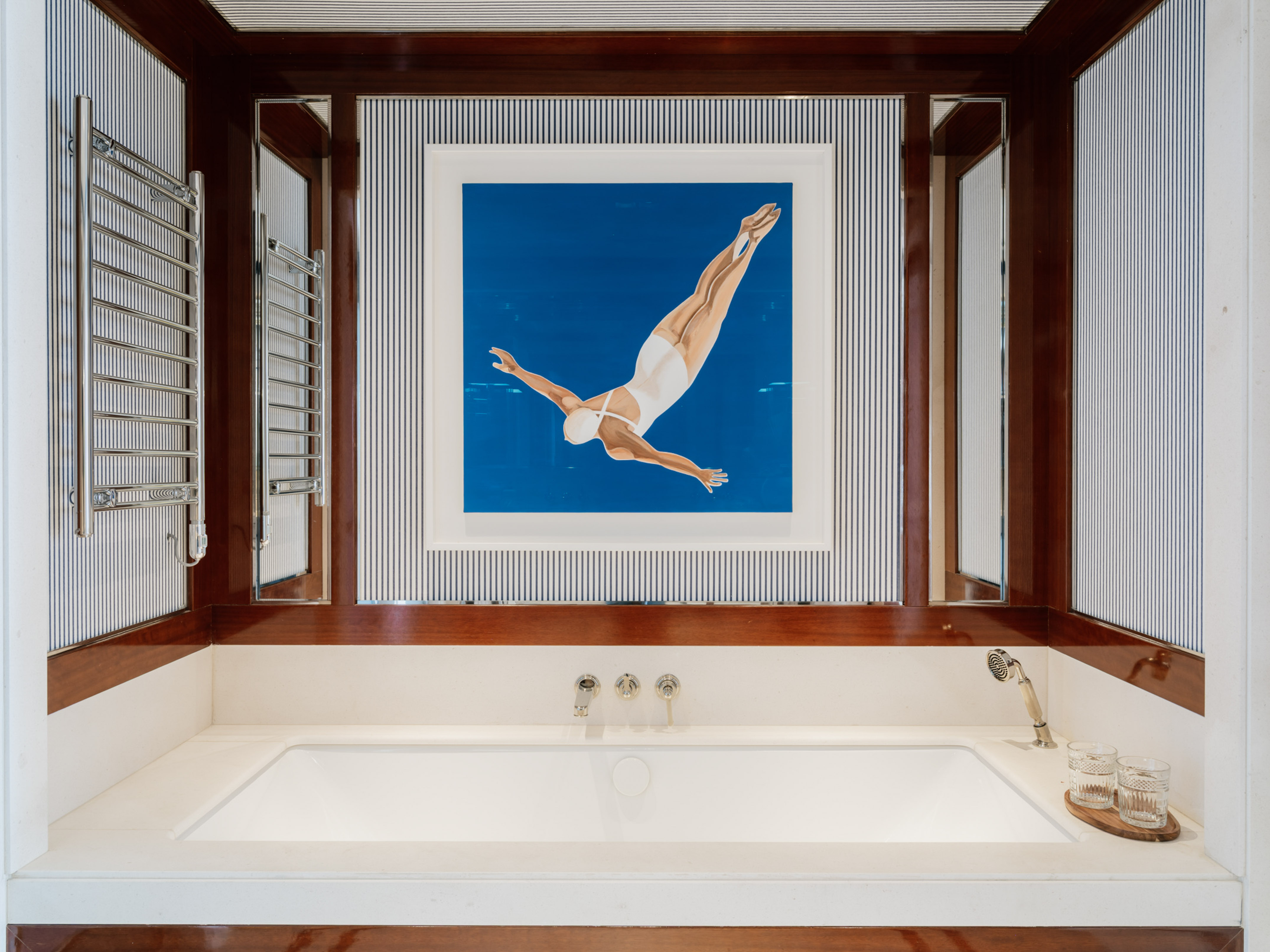 Modern bathroom features white bathtub, diver art, striped walls, and dark wood.