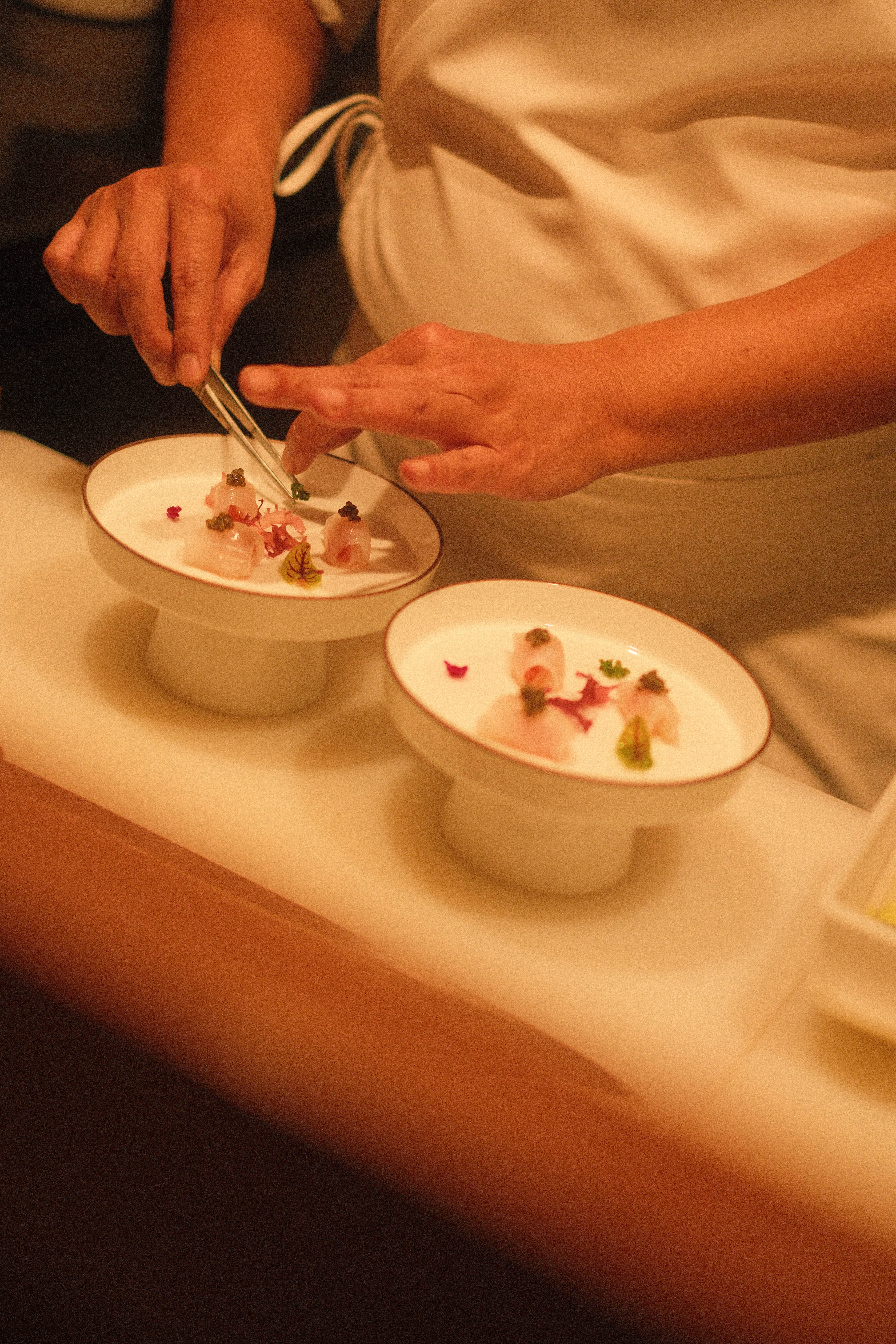 Chef plating gourmet seafood with tweezers on elegant white dishes.