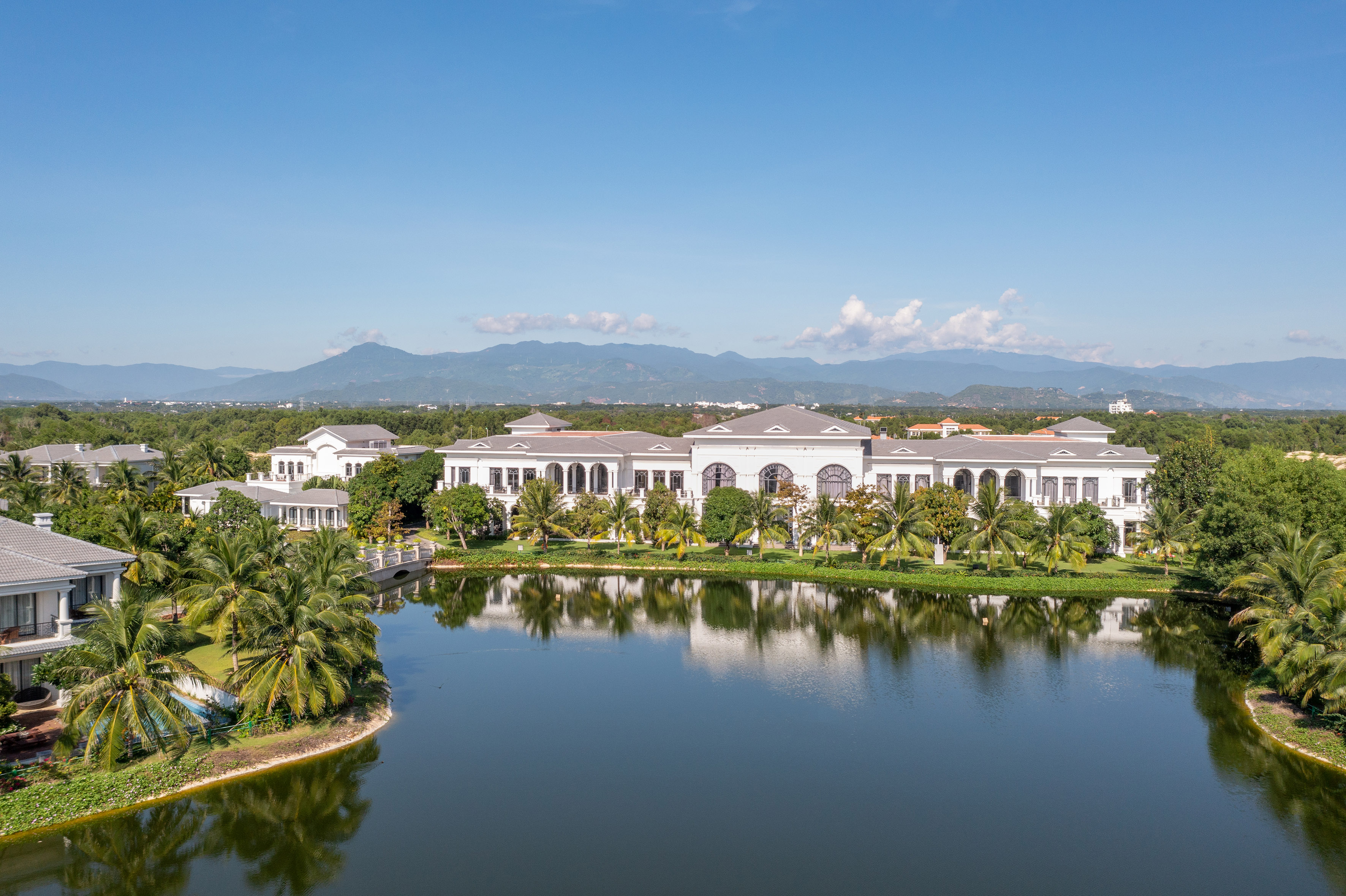 Tropical luxury resort on a reflective lake with palm trees and mountains.