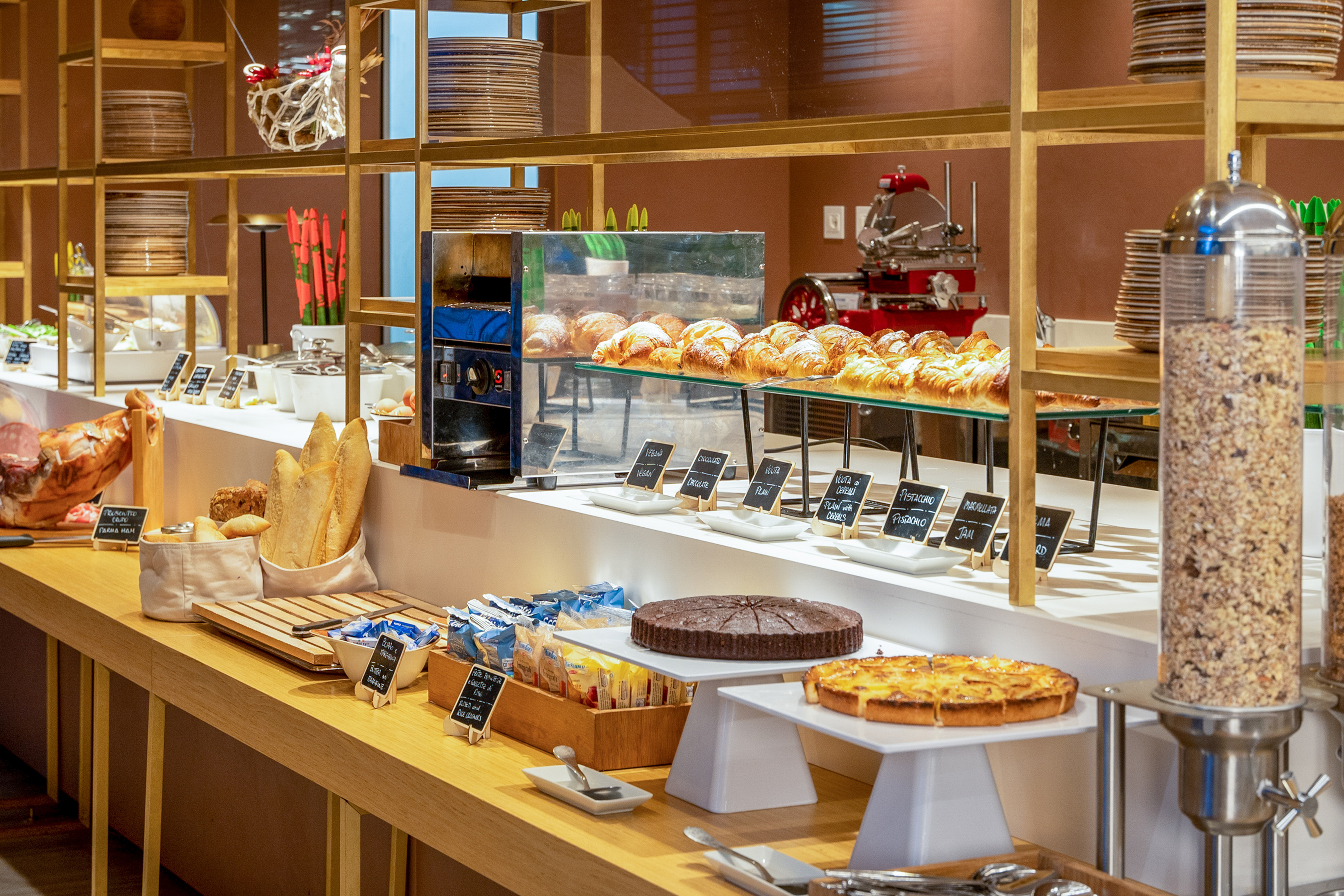 Breakfast buffet with croissants, prosciutto, breads, pastries, and cereals.