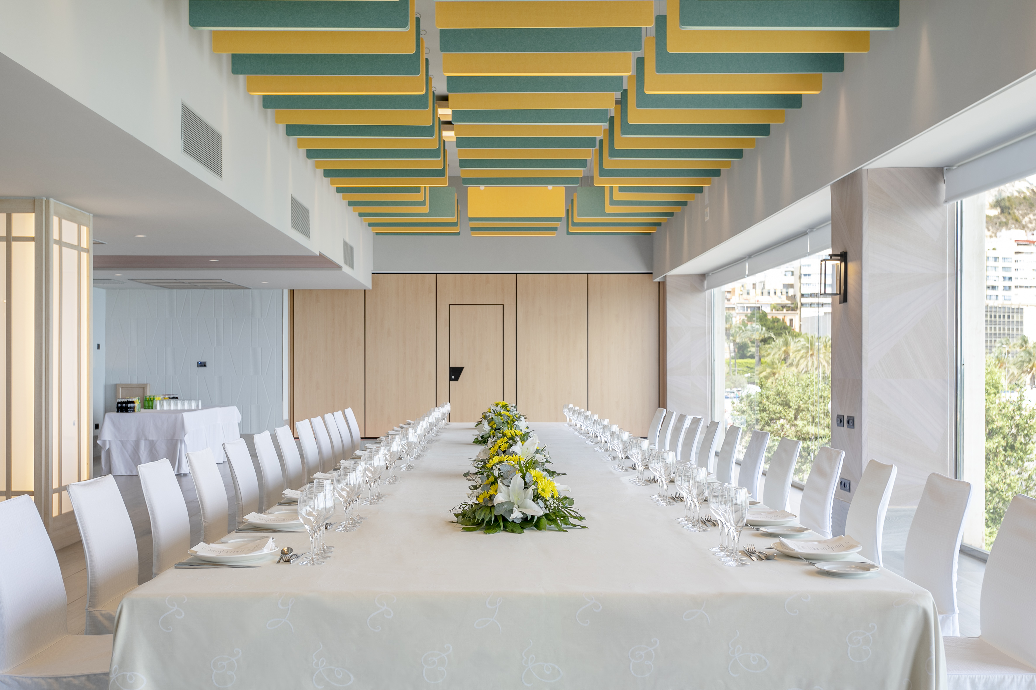 Formal dining room with long table, flowers, and green-yellow ceiling panels.