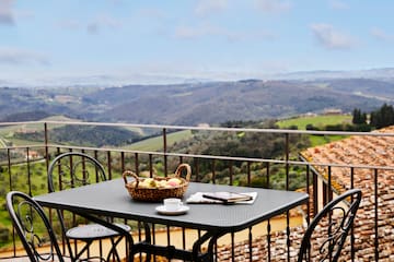 a table with a basket of fruit and a cup on a balcony overlooking a valley
