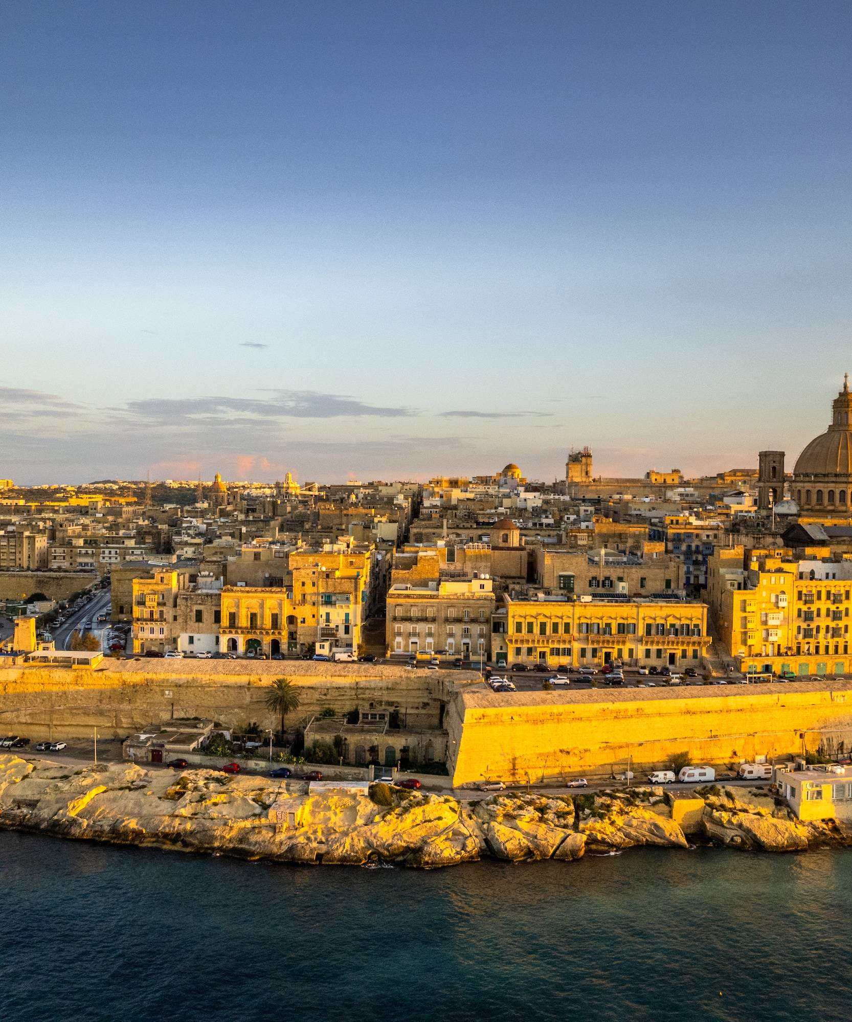 Valletta, Malta cityscape and historic fortifications at sunset over the harbor.