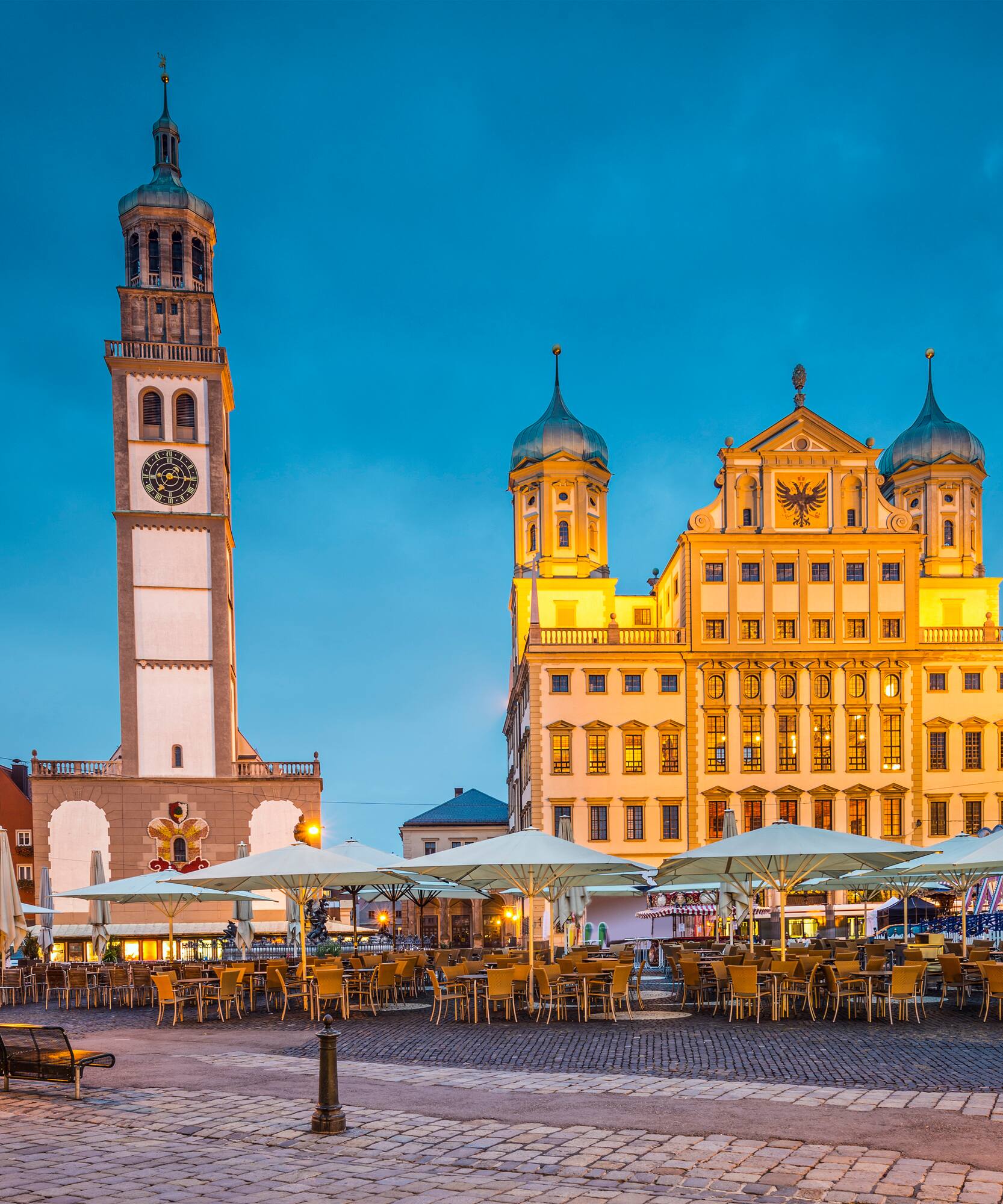 Augsburg Rathaus, Perlachturm and outdoor cafes on cobblestone square at dusk.