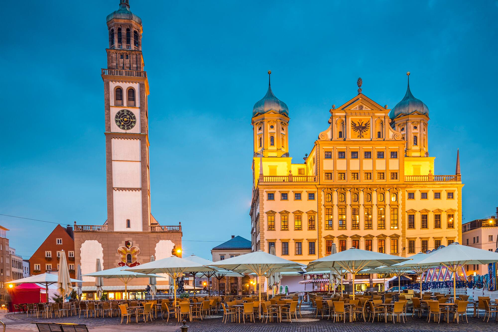 Augsburg Rathaus, Perlachturm and outdoor cafes on cobblestone square at dusk.