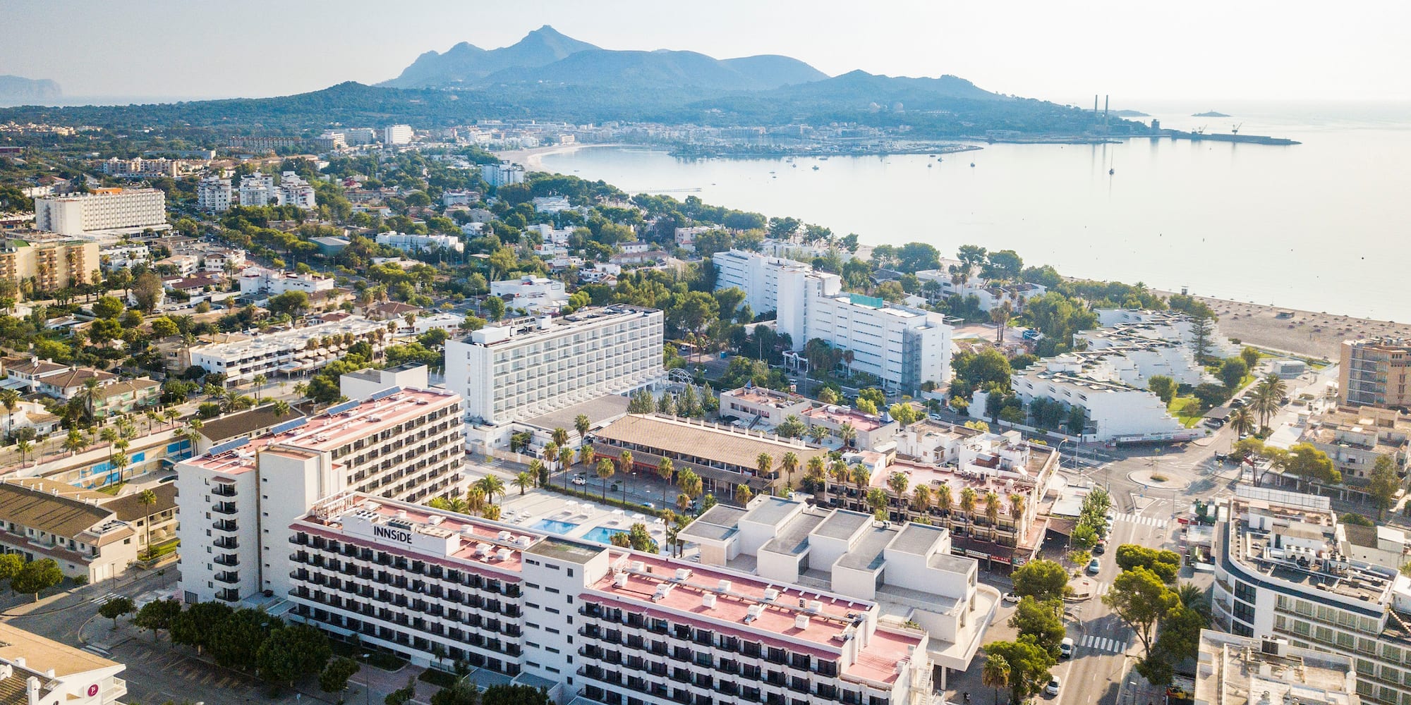Innside hotel, coastal resort town, beach, bay, and mountains under clear sky.