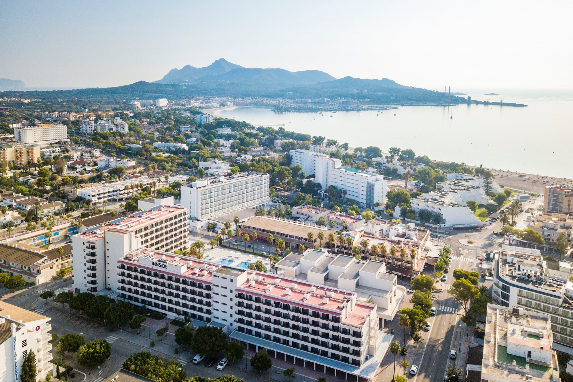 Innside hotel, coastal resort town, beach, bay, and mountains under clear sky.