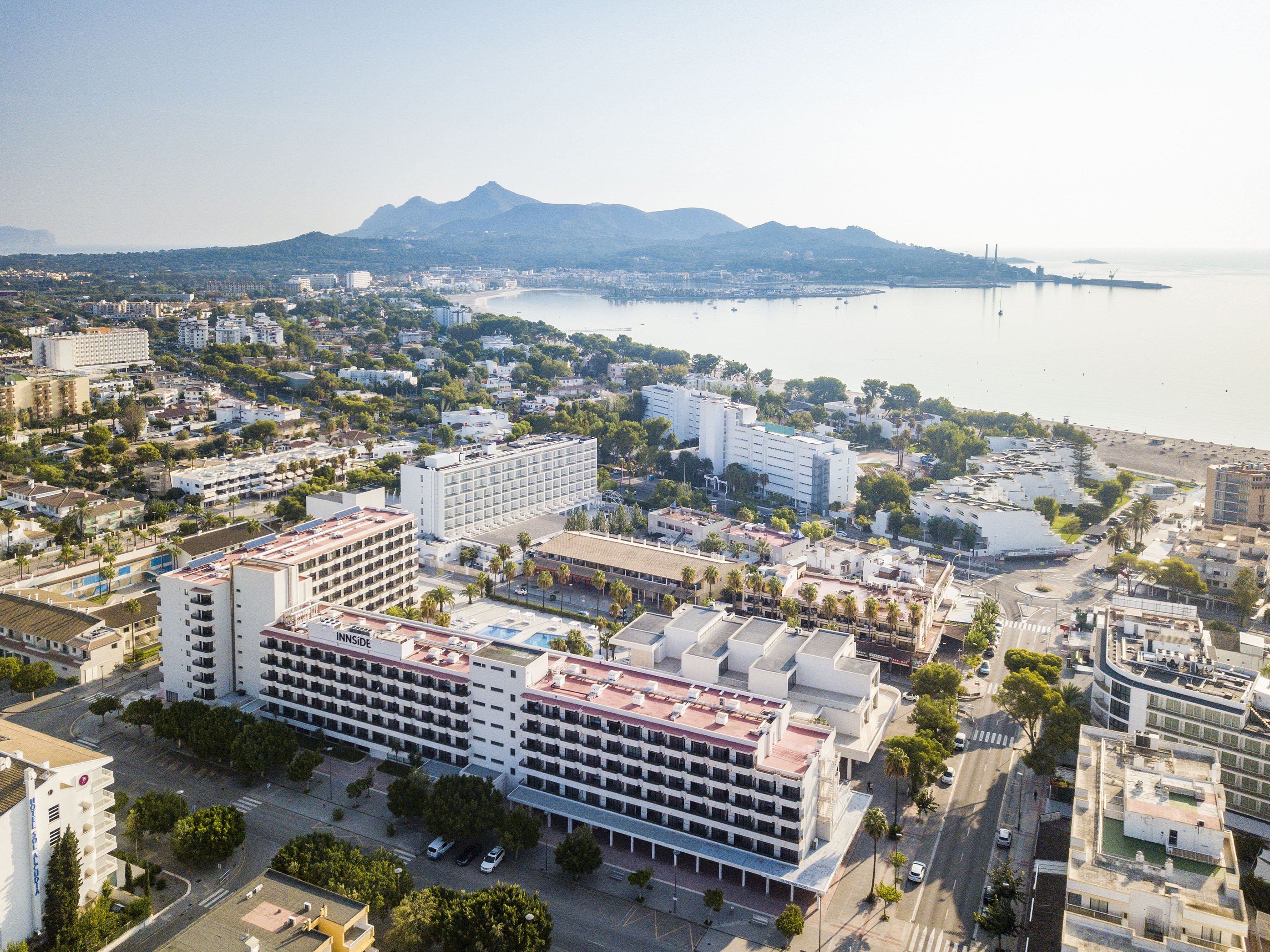 Innside hotel, coastal resort town, beach, bay, and mountains under clear sky.