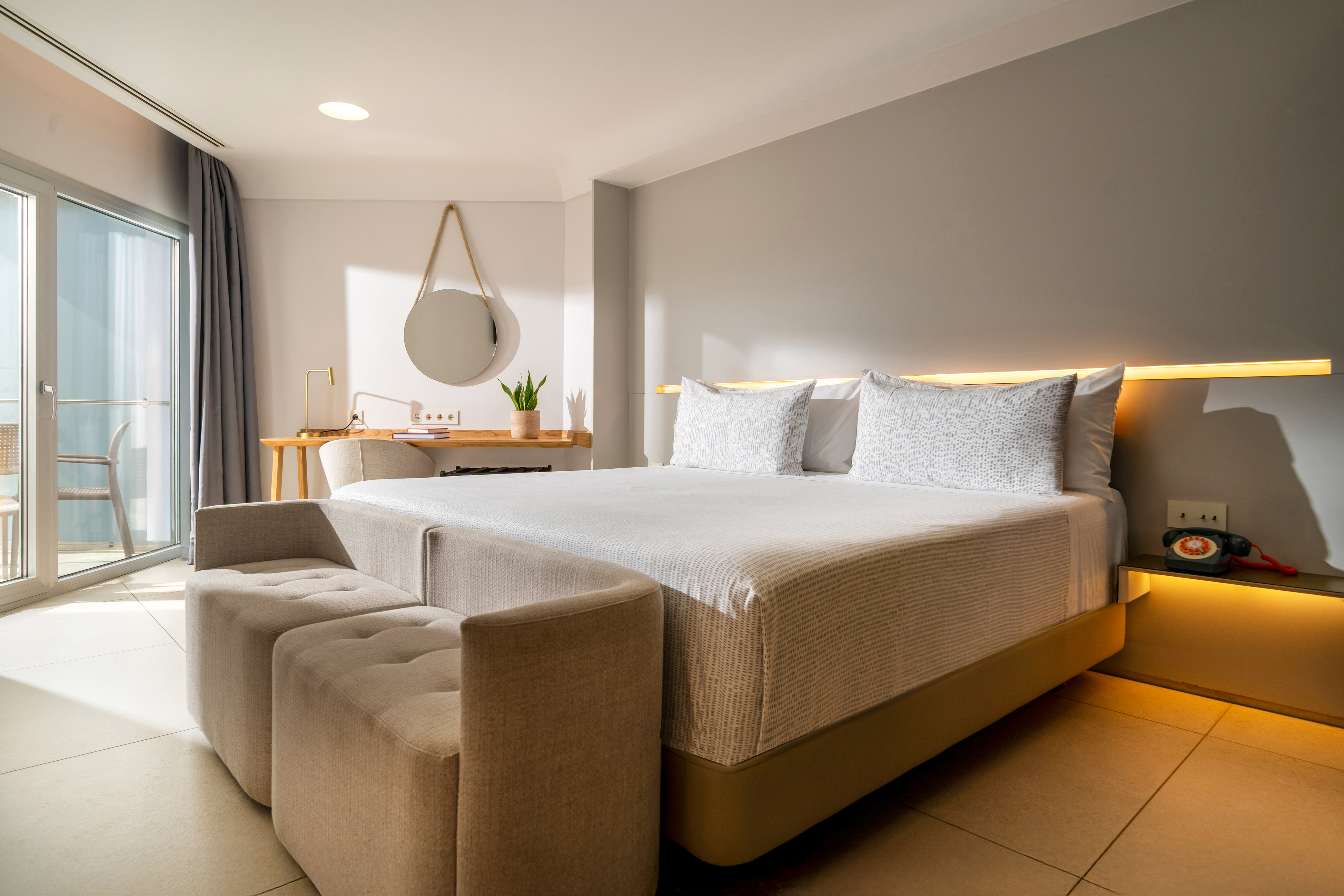 Bright modern hotel bedroom with bed, desk, sofa, and balcony access.