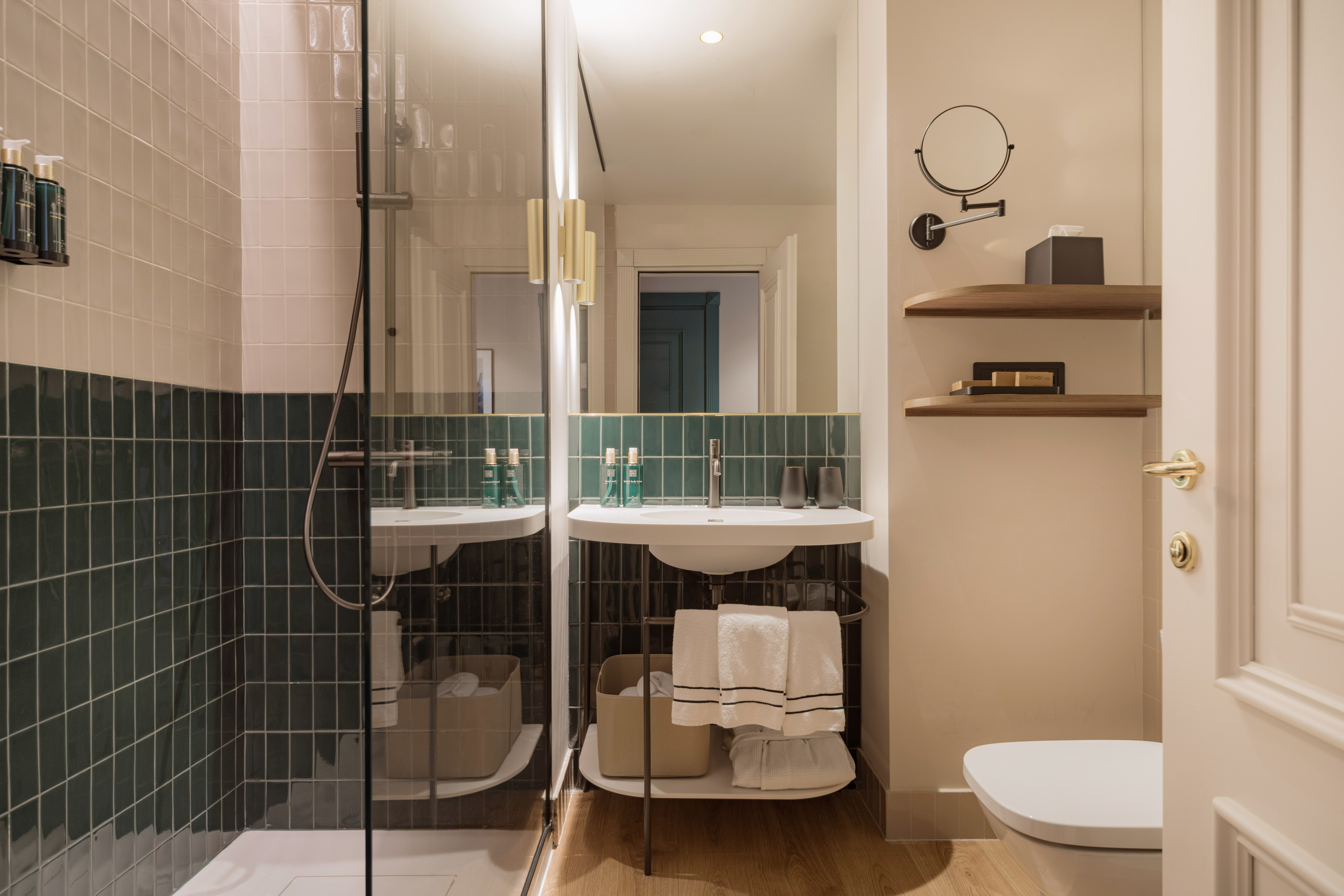 Modern hotel bathroom with green tiled shower, white vanity, and mirror.