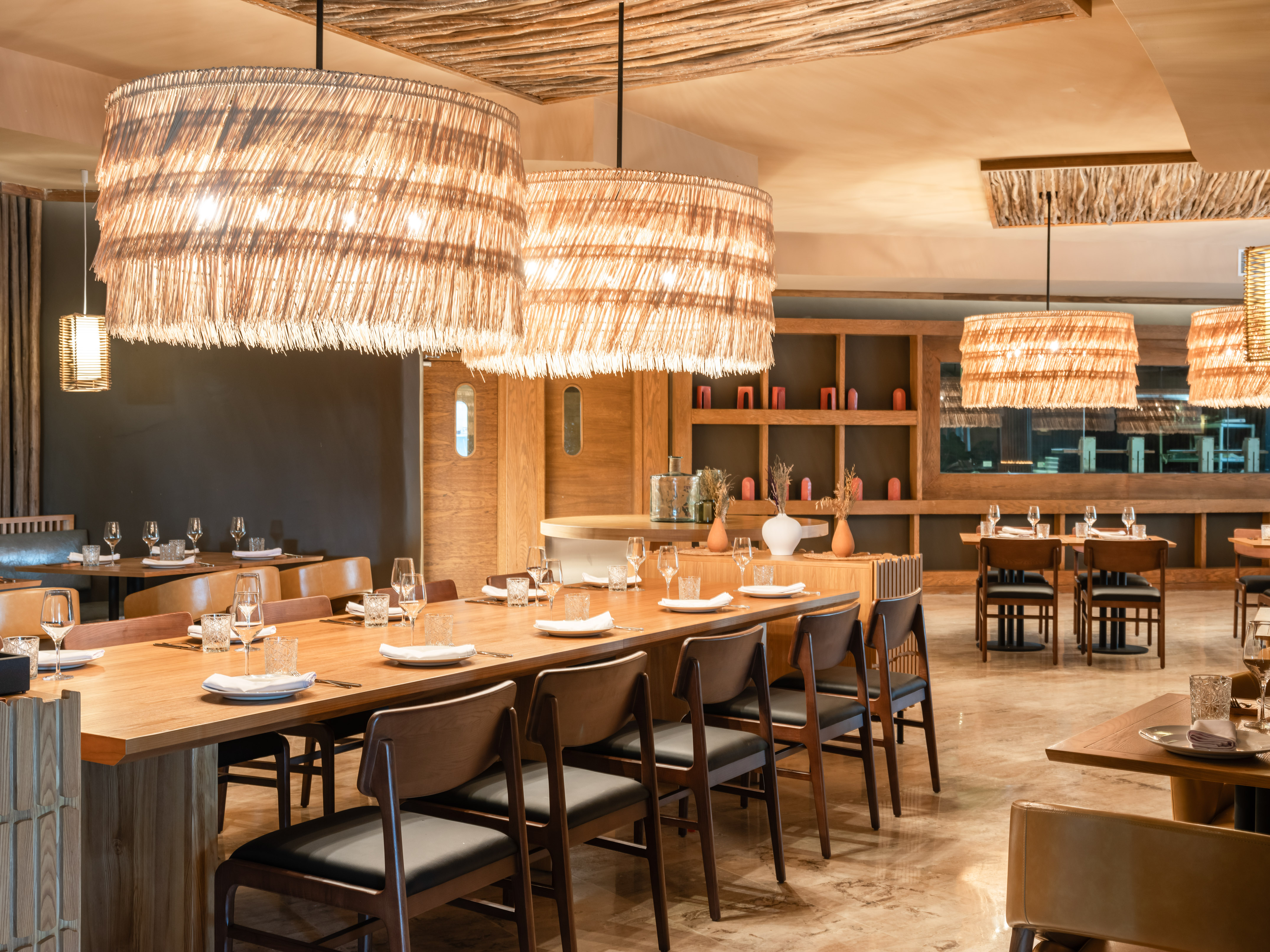 Restaurant dining room with long wooden table and natural woven lights.