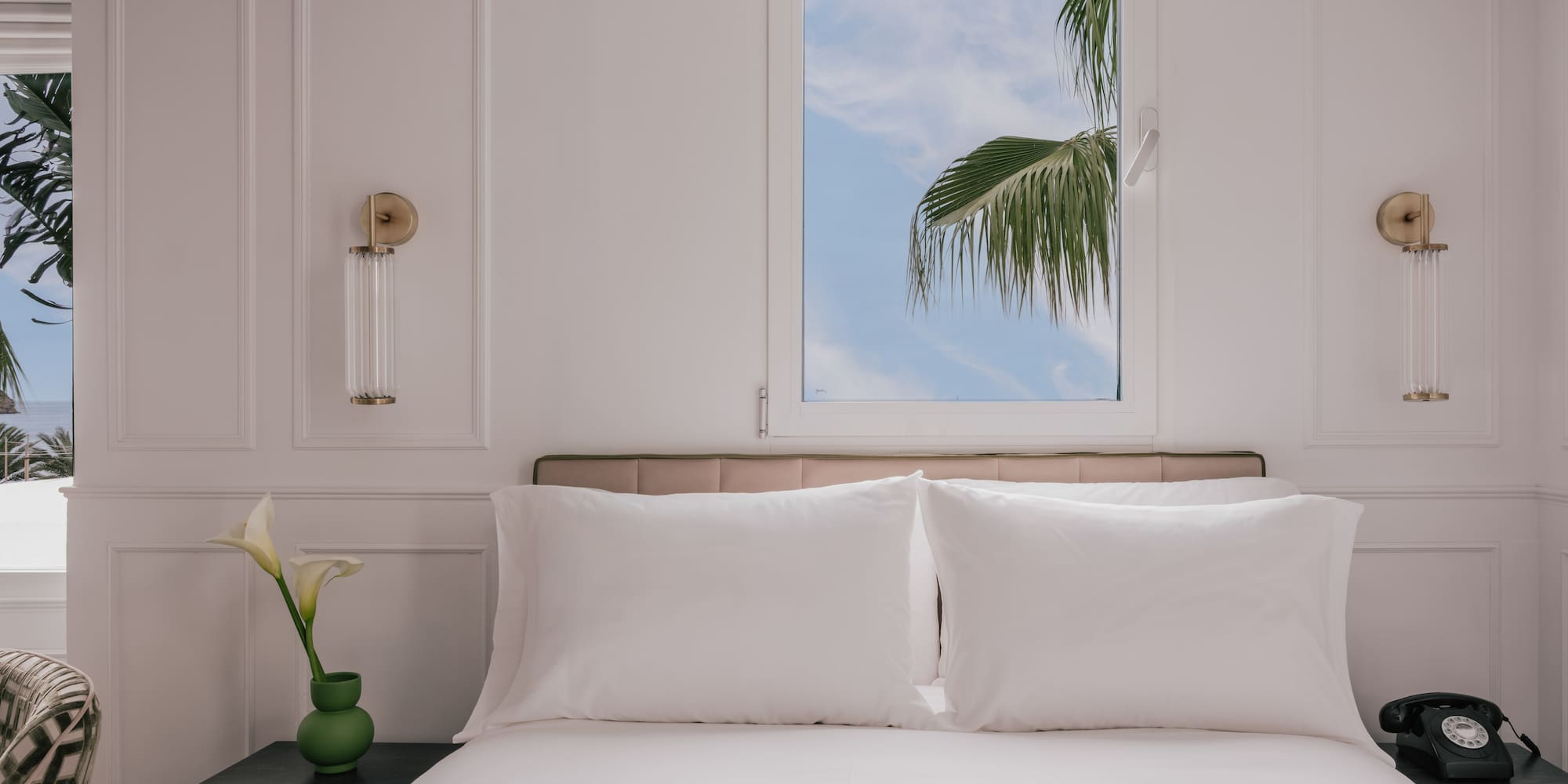Hotel bedroom with white bed, palm tree outside window, bedside phone.