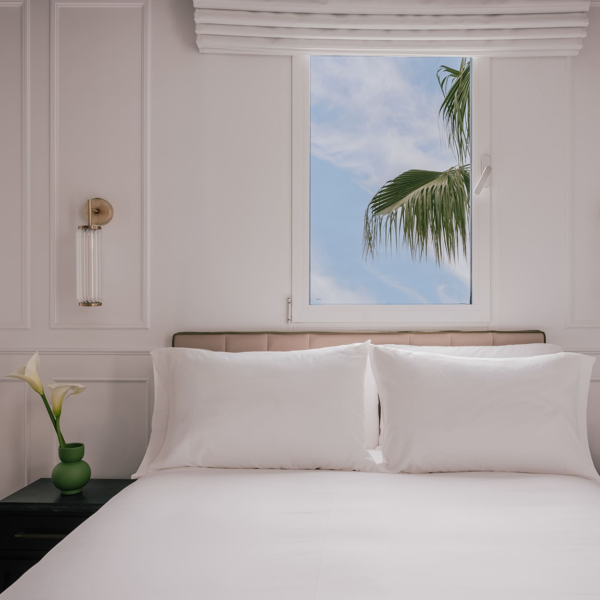 Hotel bedroom with white bed, palm tree outside window, bedside phone.