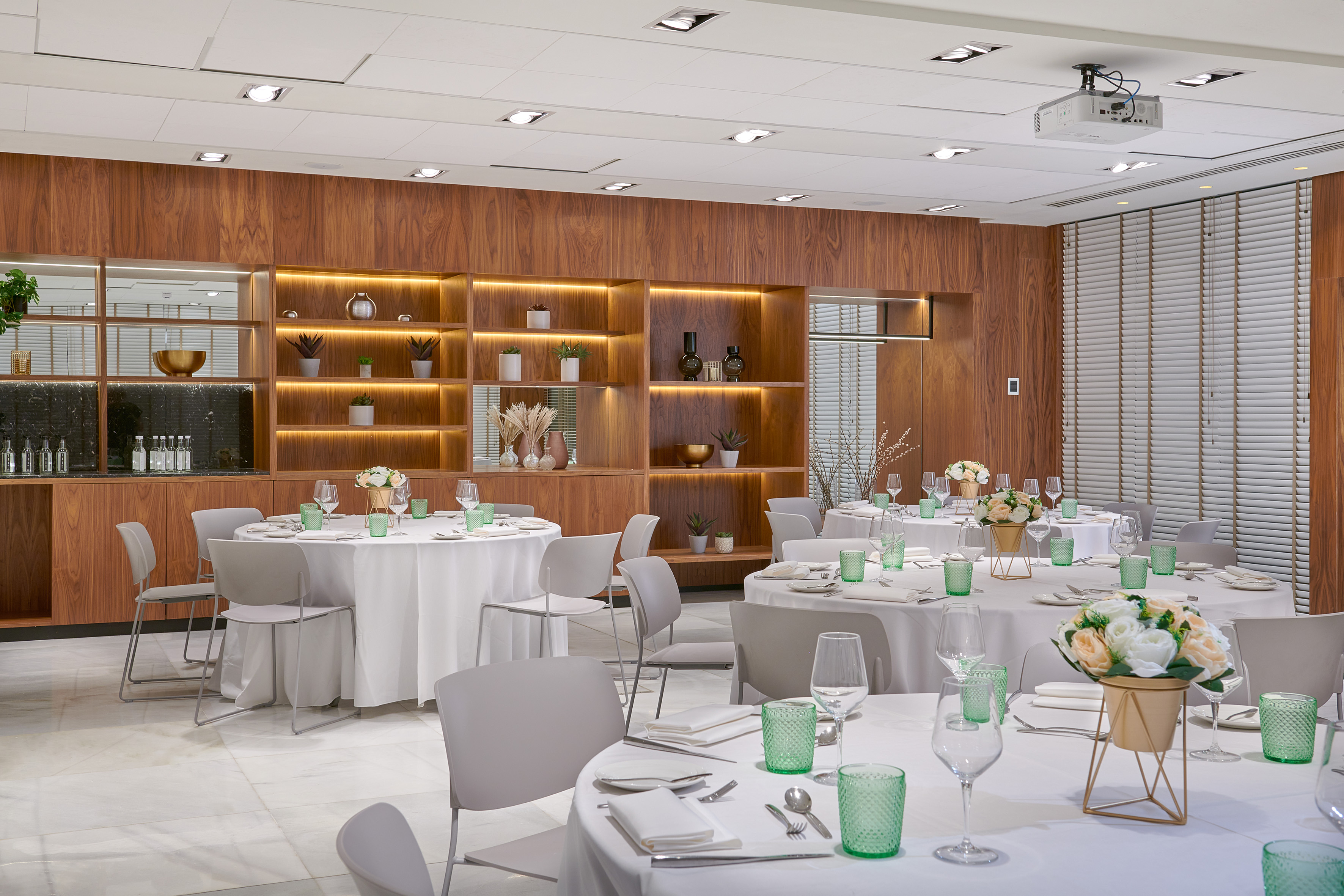Modern event room with set tables, green glasses, flowers, wood accents.